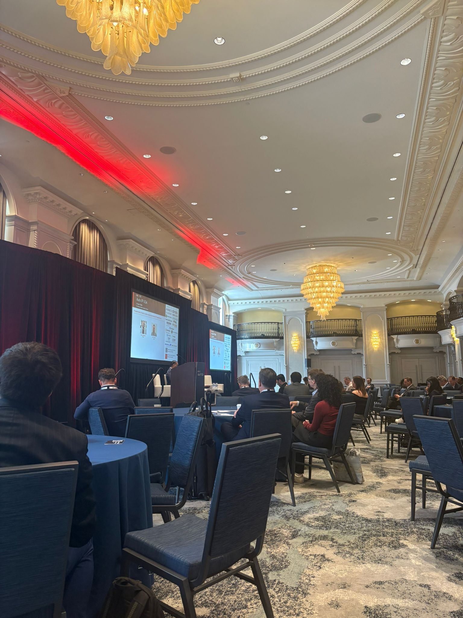 Conference ballroom audience seated at round tables watching a presentation on stage at the Auto IP USA event