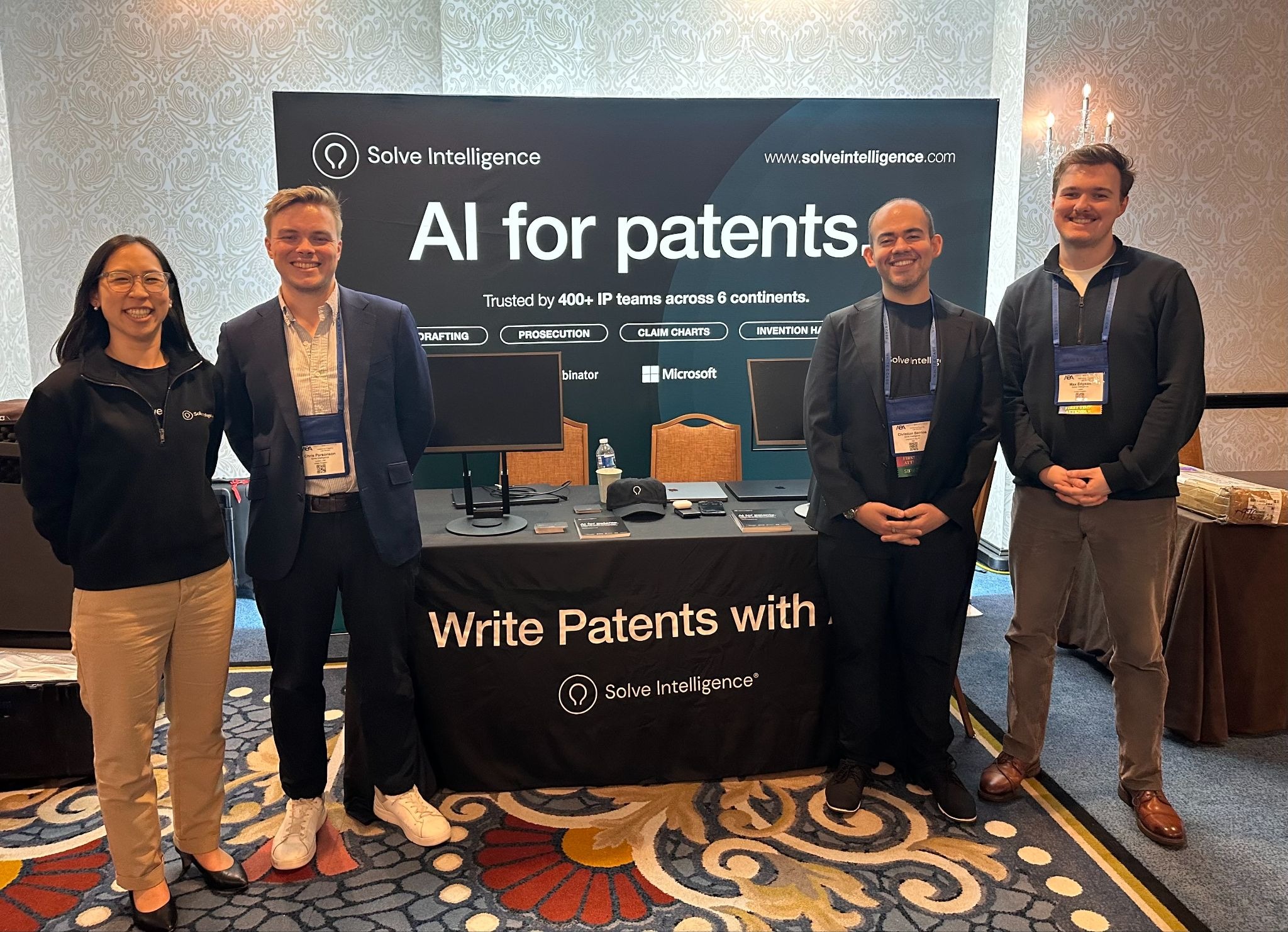 Four people posing at a conference booth in front of a “Solve Intelligence — AI for patents” banner reading “Write Patents with AI”