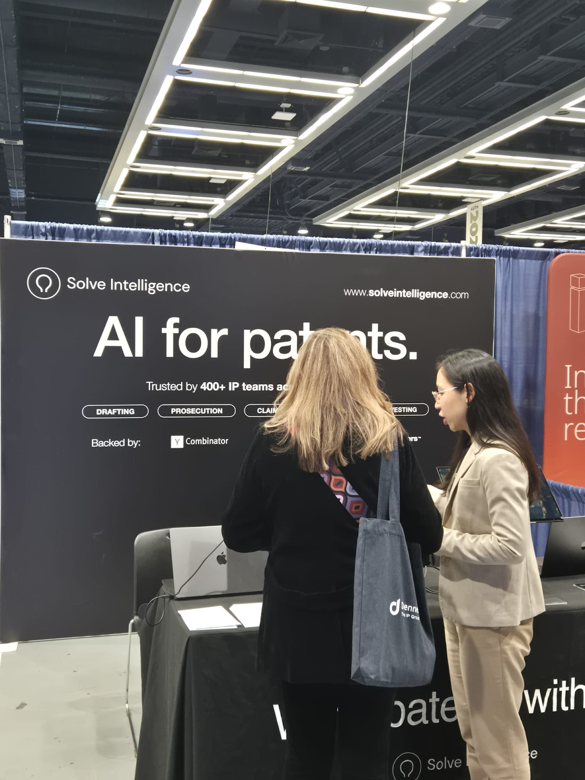 Two people talking at the Solve Intelligence booth in front of a banner reading “AI for patents,” trusted by 400+ IP teams