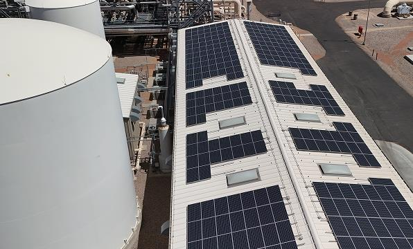 Commercial rooftop solar arrays beside storage tanks at an industrial facility