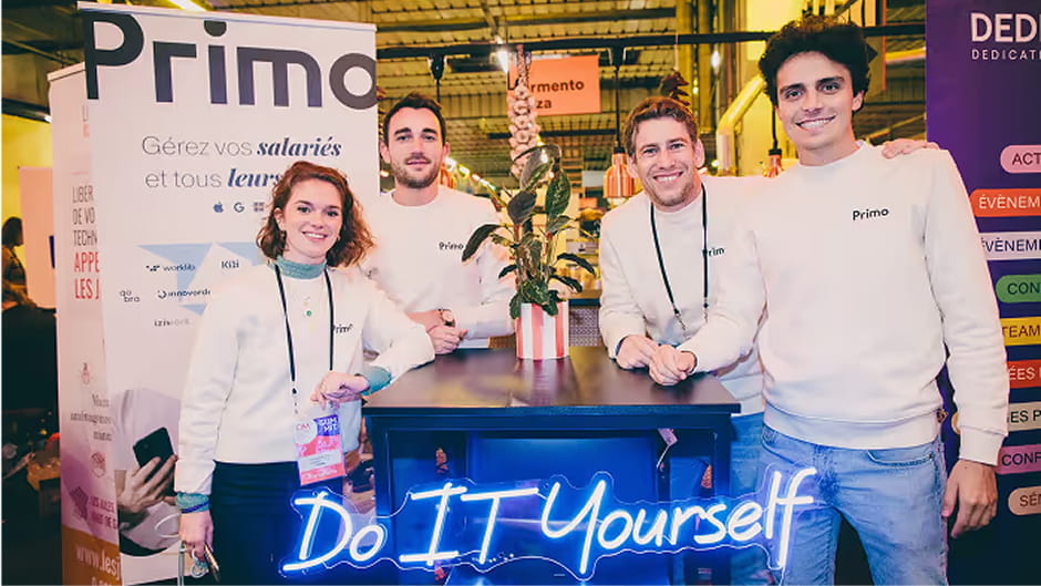 Des membres de l'équipe Primo sur leur stand, sous un néon « Do IT Yourself »