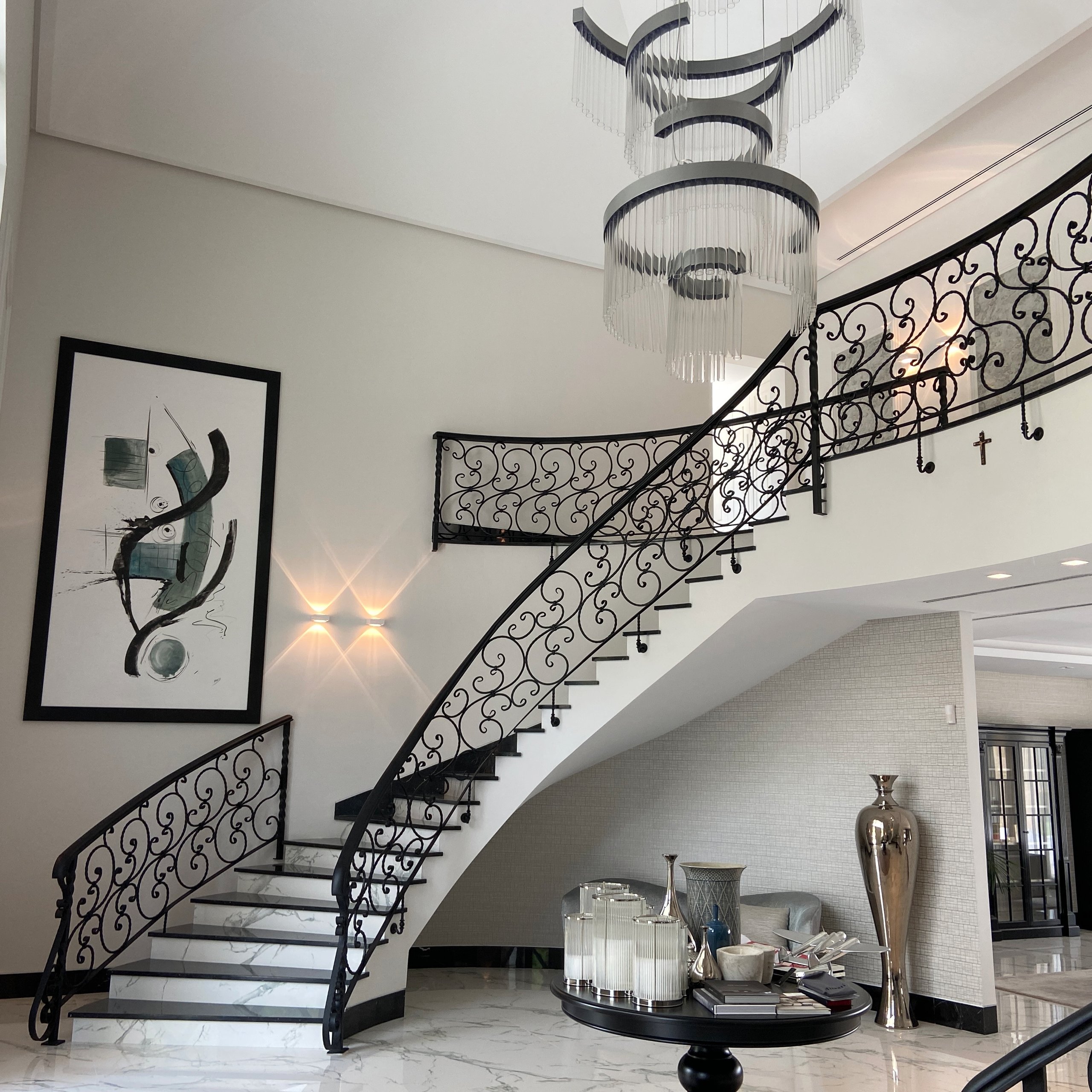 Staircase with decorative railings, chandelier and wall lighting