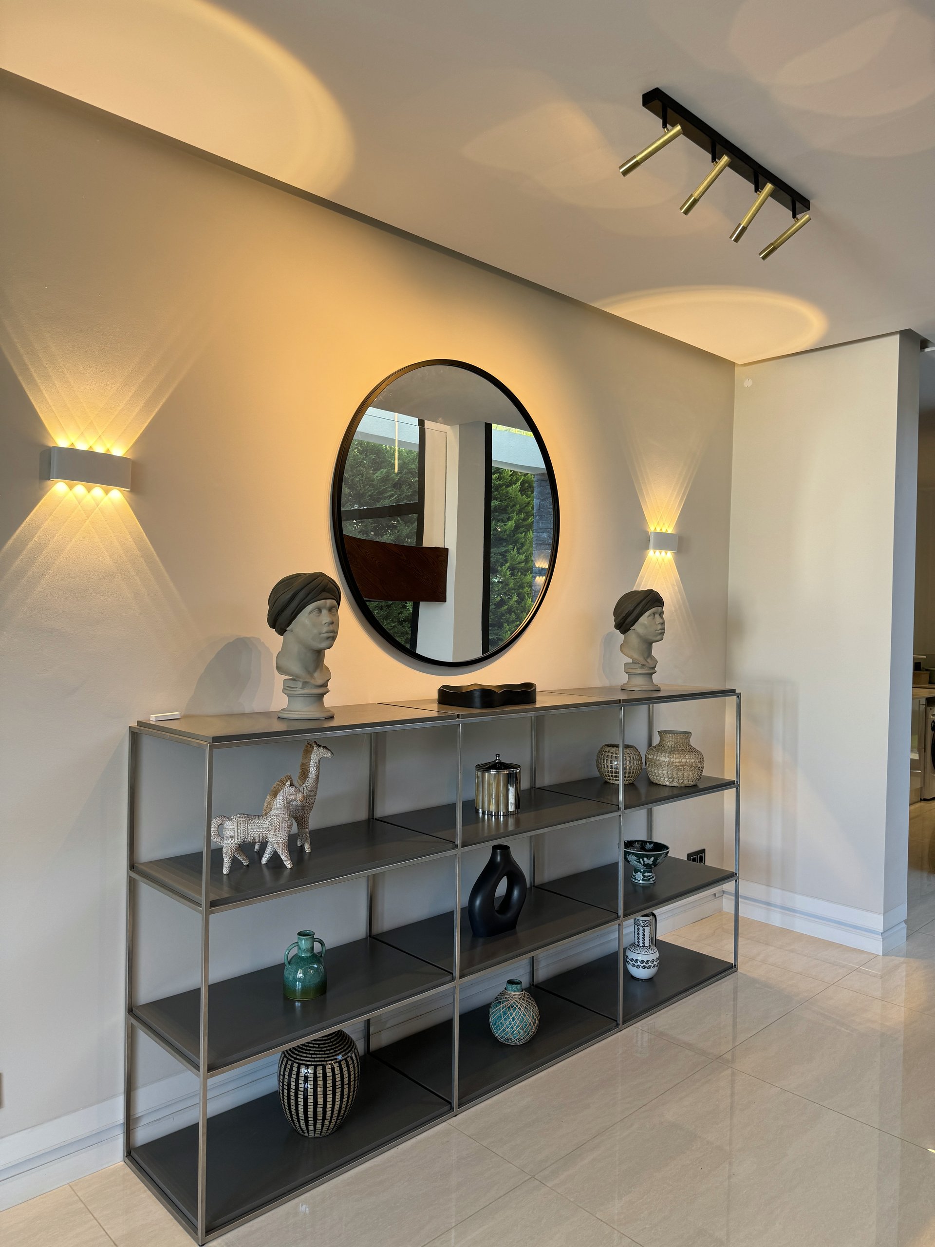 Warm wall lighting beside a round mirror and display console