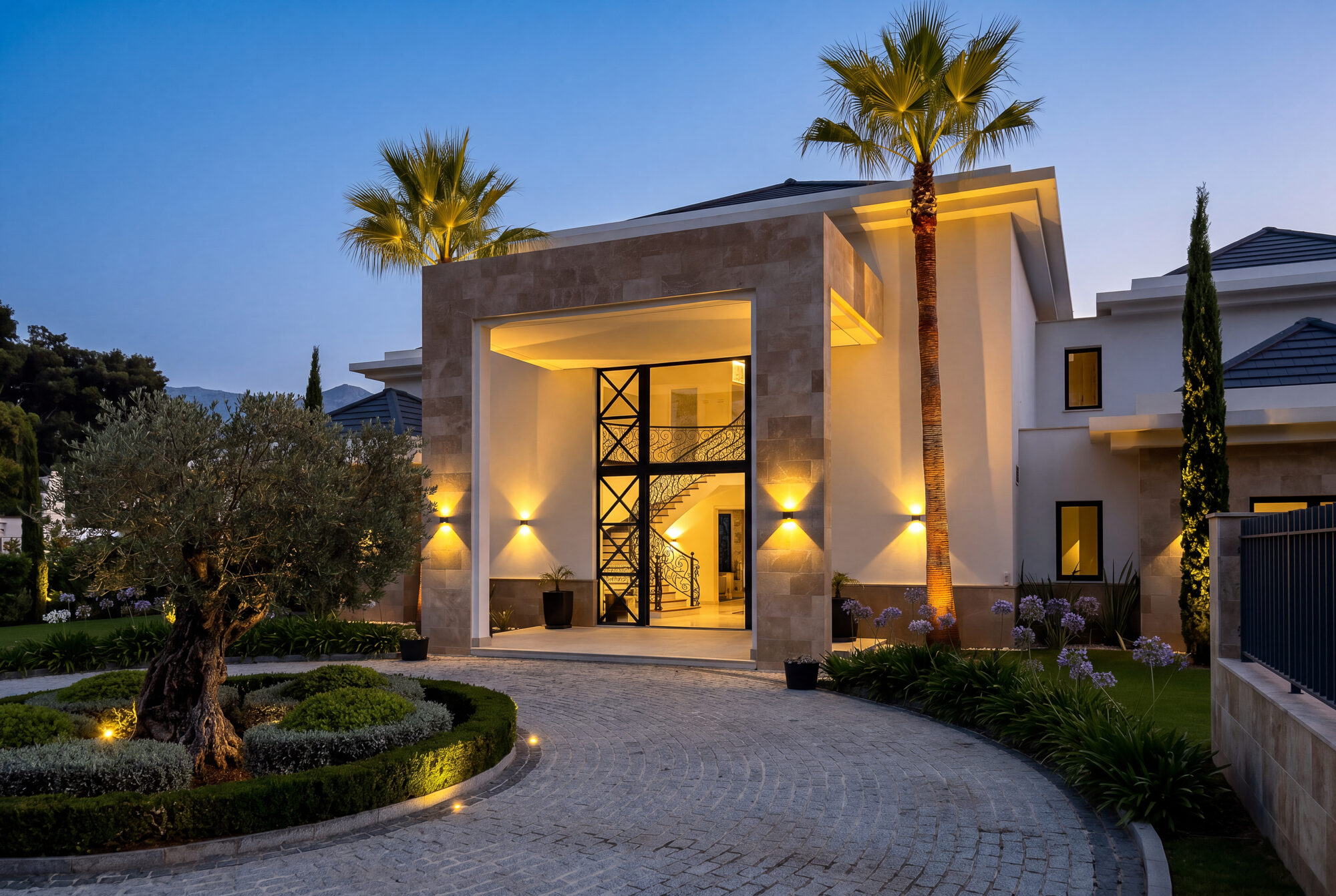 Front entrance and landscaped driveway of a modern villa illuminated at dusk