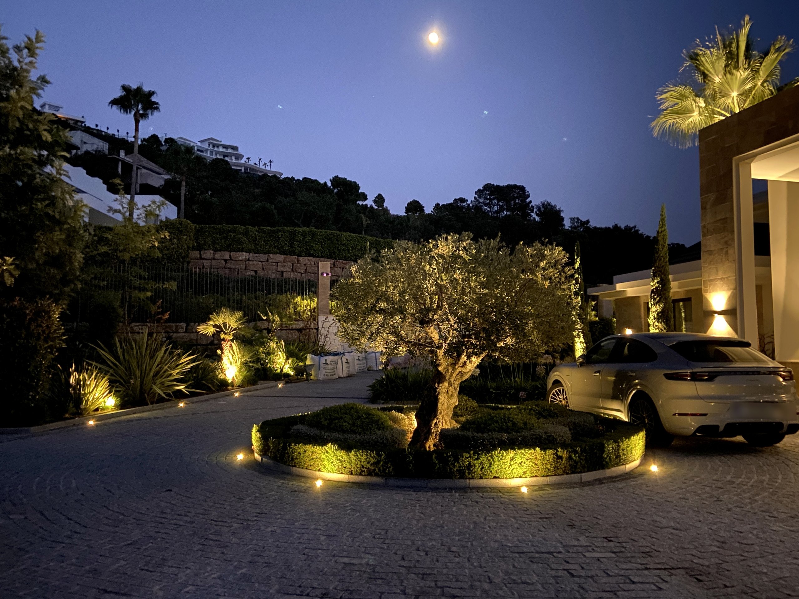 Illuminated driveway, landscaped roundabout and villa entrance at dusk