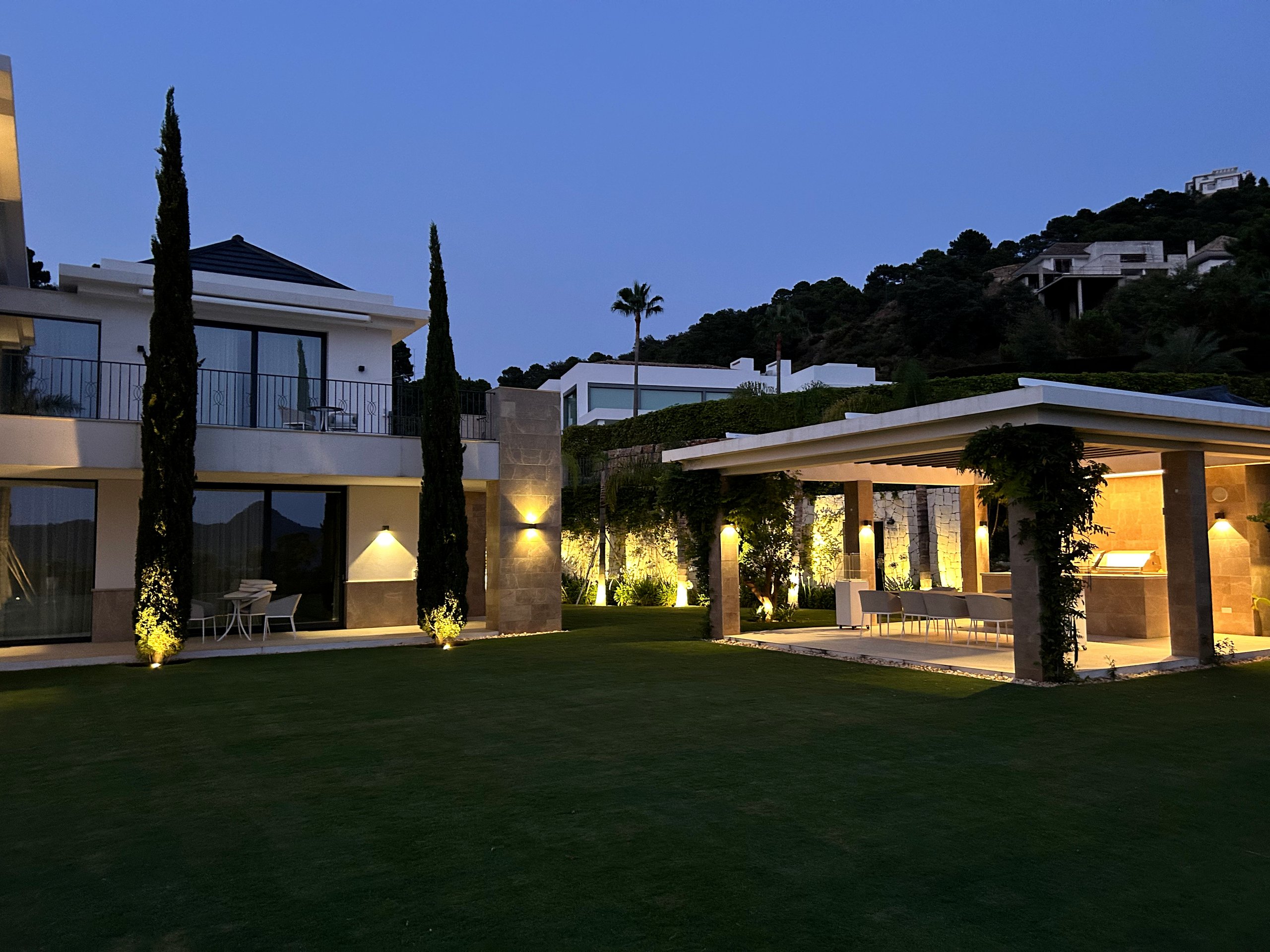 Wide garden view of a modern villa with architectural lighting at dusk