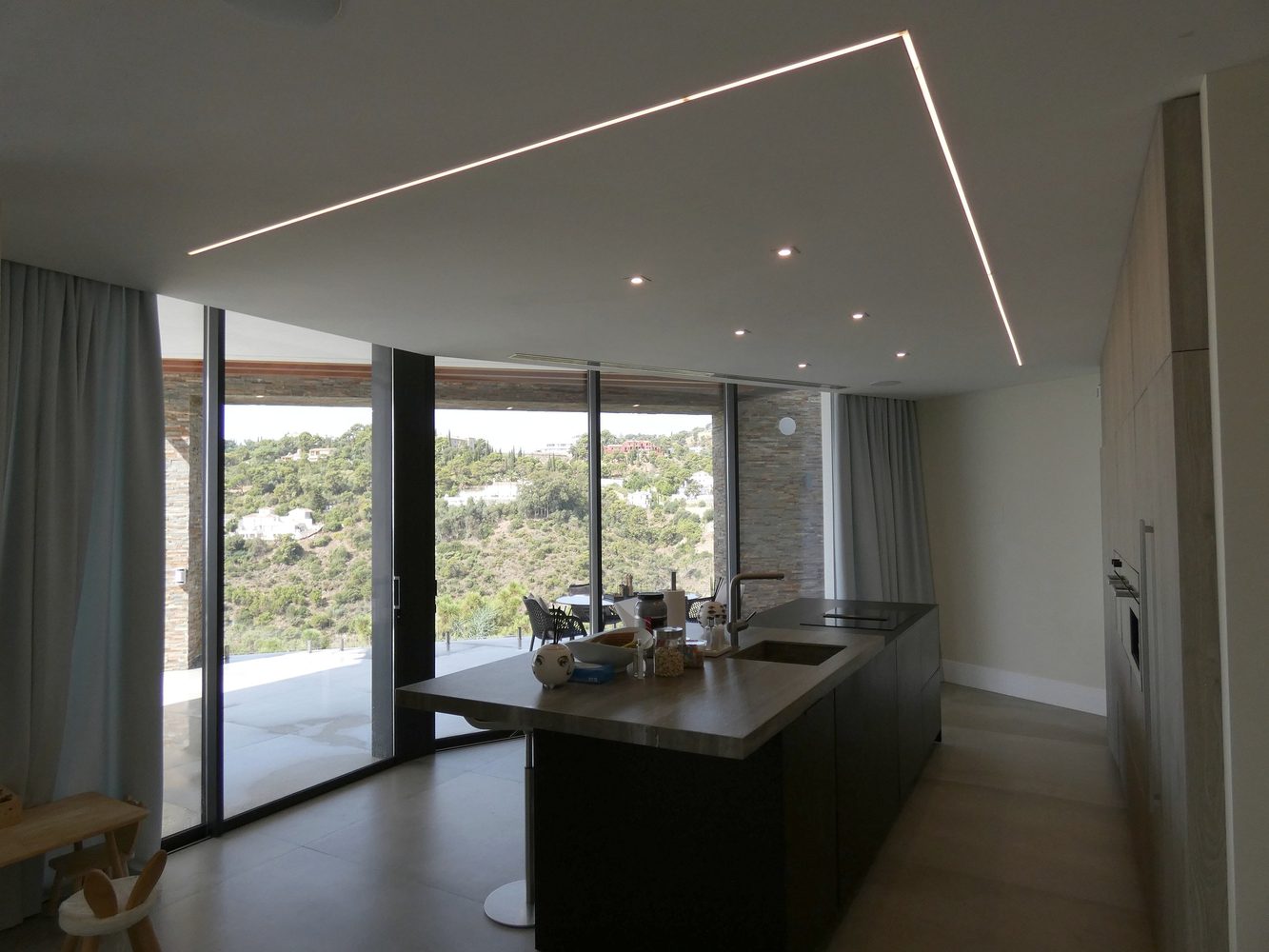 Modern kitchen with linear ceiling lighting and garden views