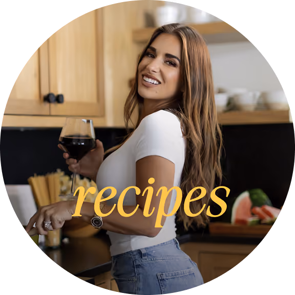 Smiling woman holding a glass of red wine in a kitchen with wooden cabinets.