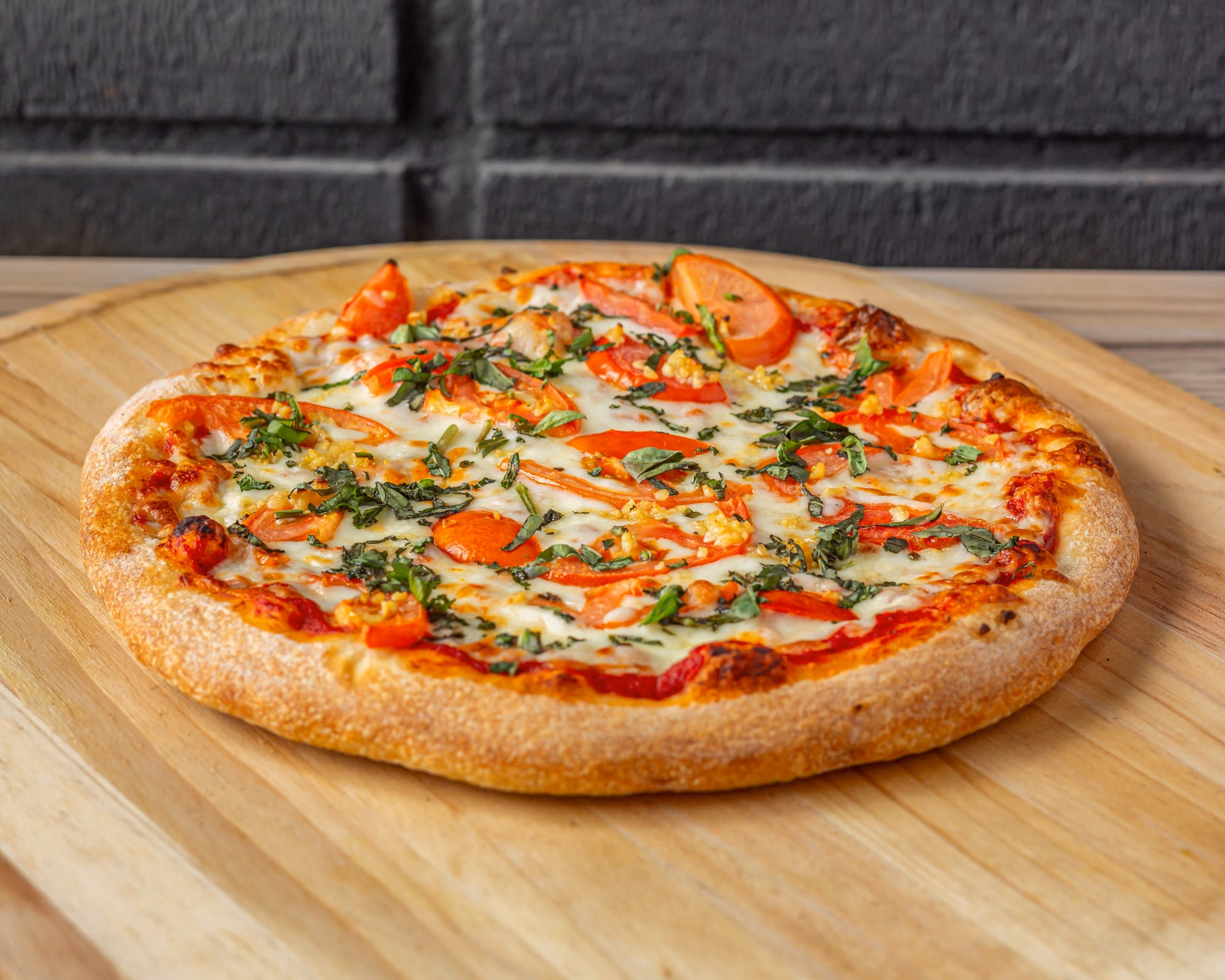 Whole pizza with tomato, melted cheese, garlic, and herbs on a wooden board.