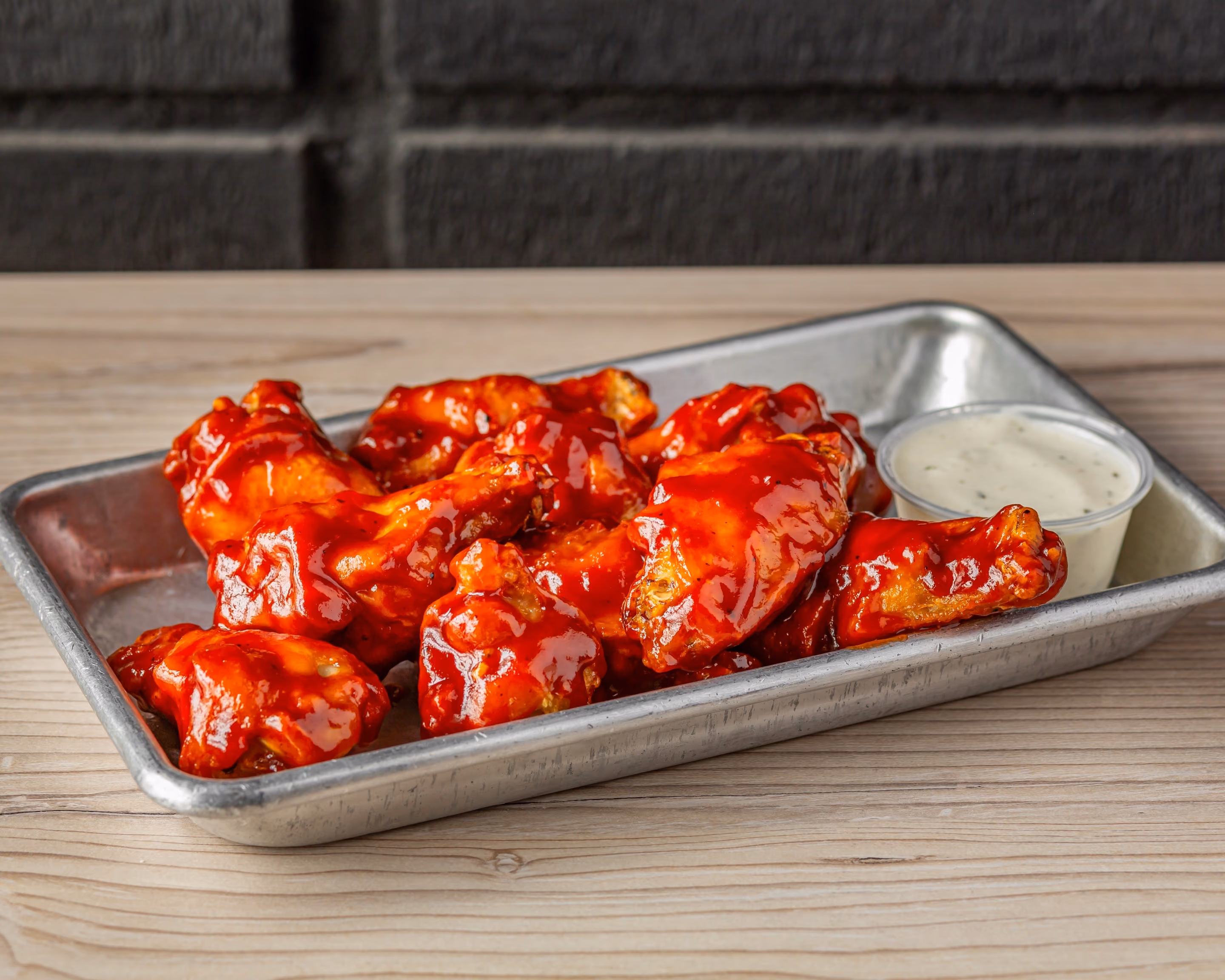 Tray of saucy buffalo chicken wings with a side of ranch dressing on a wooden table.