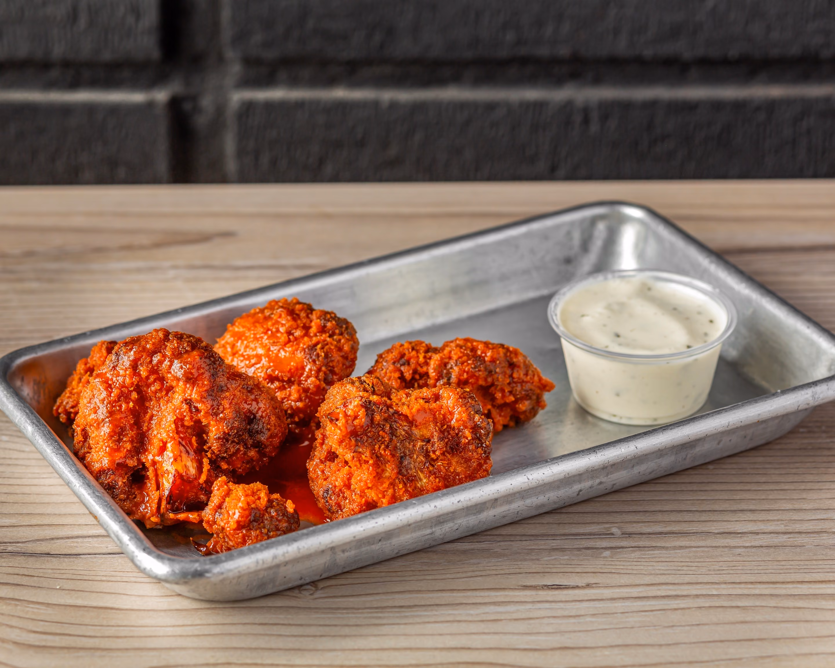 Tray with spicy fried cauliflower bites and a cup of creamy dipping sauce on a wooden table.