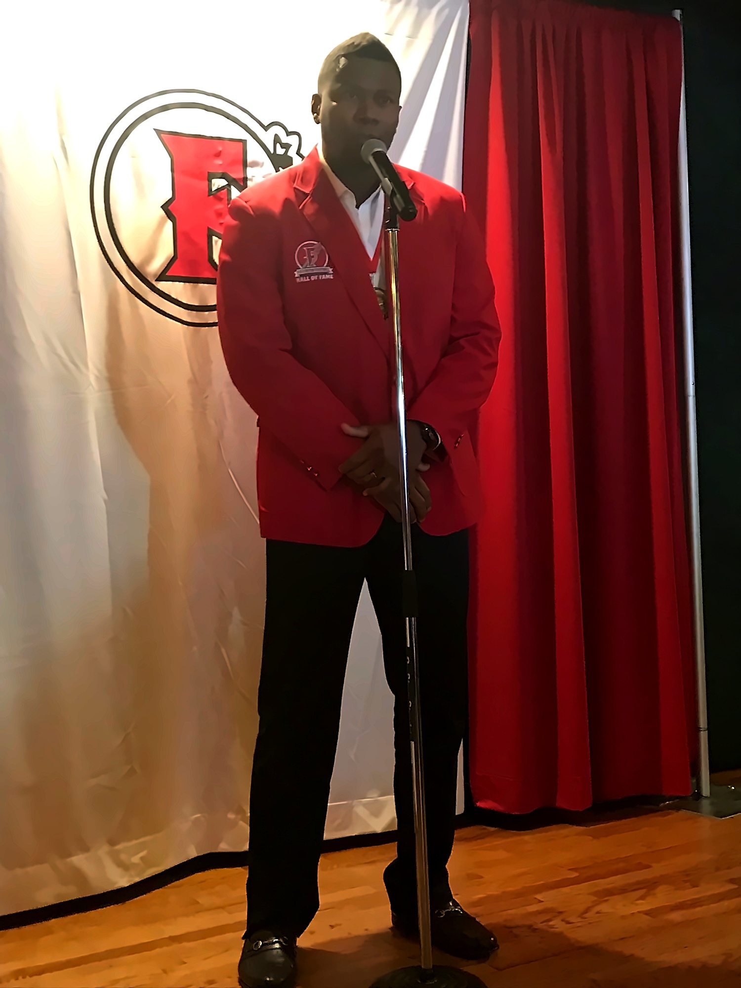 Daniel Fells speaking at the podium in red jacket