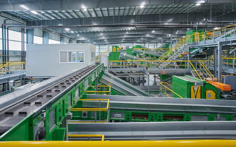 Interior of a material recovery facility with green sorting conveyors and elevated walkways
