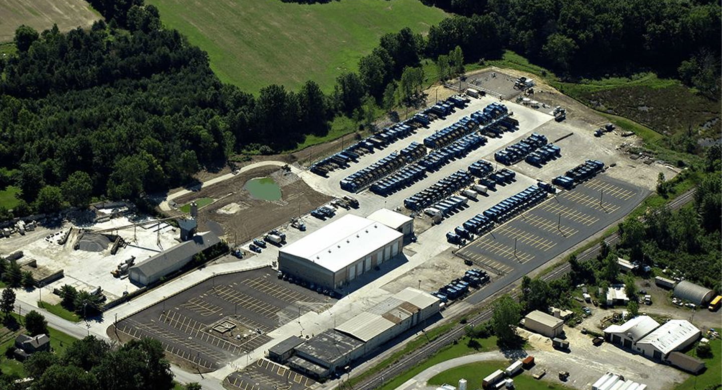 Aerial view of a hauling facility with rows of collection trucks beside wooded farmland
