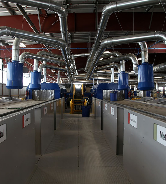Interior of a processing facility with blue air-handling cyclones over labelled sorting bunkers