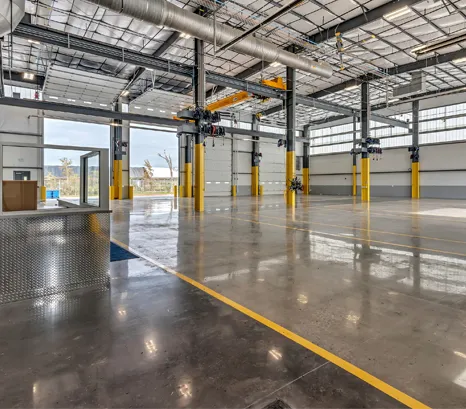 n expansive, well-equipped maintenance facility supporting a modern waste hauling fleet. The interior features multiple service bays designed to accommodate heavy-duty collection vehicles, with technicians performing routine inspections, preventative maintenance, repairs, and equipment servicing.