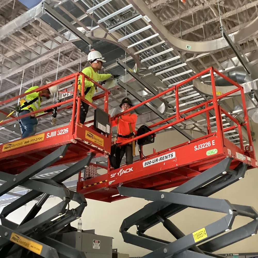 Construction workers working on ceiling duct installation on scissor lifts inside a building under construction for the solid waste industry.
