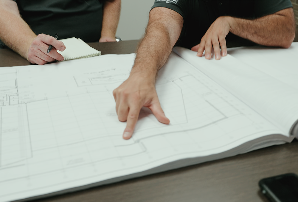 Two people review architectural blueprints on a table for a design-build project.