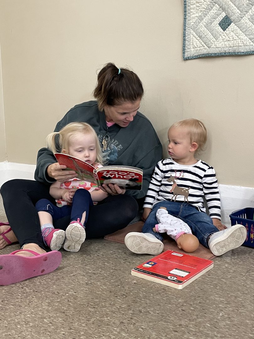Toddlers reading with their educator on the classroom couch