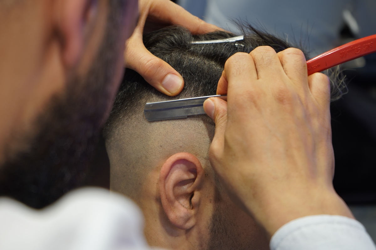 A close-up view of a barber shaving a man's hair with a straight razor at Hammer & Nails, Texas