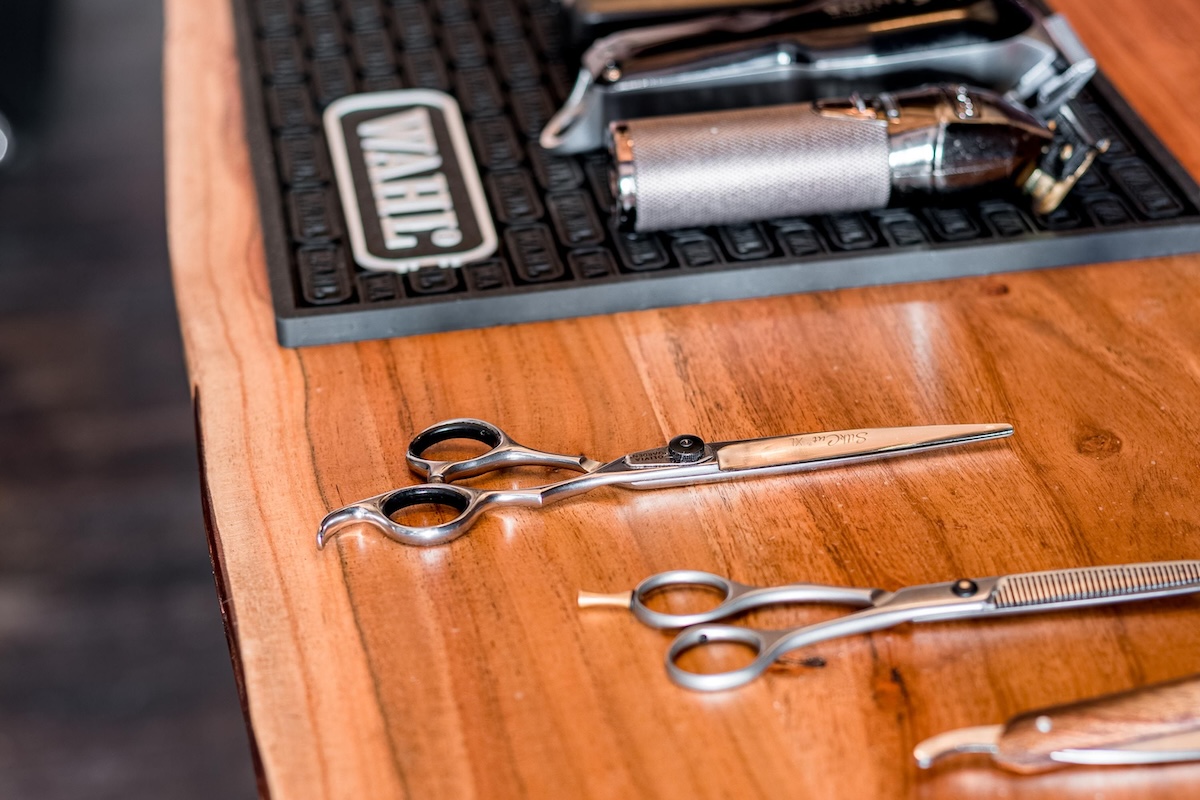Close-up of barber tools including scissors and electric shavers laid out on a wooden table.