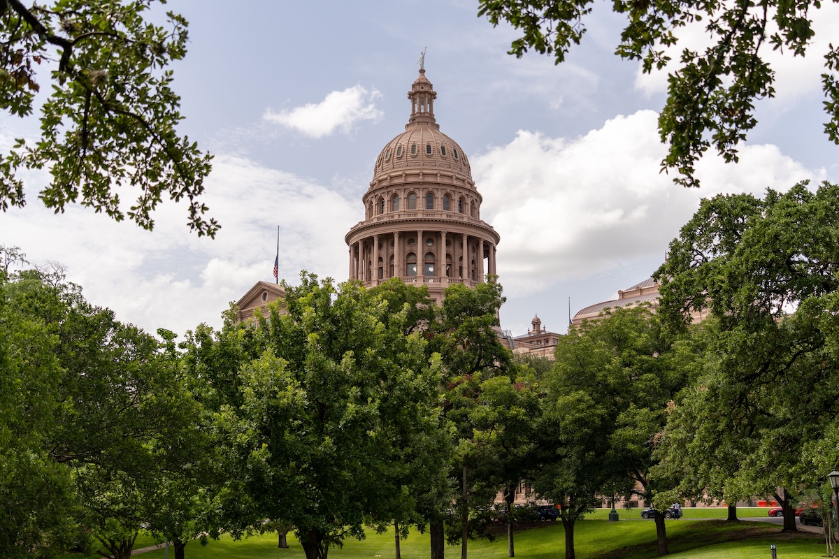 View of the Texas State Capitol dome amidst lush greenery on a sunny day in Austin.