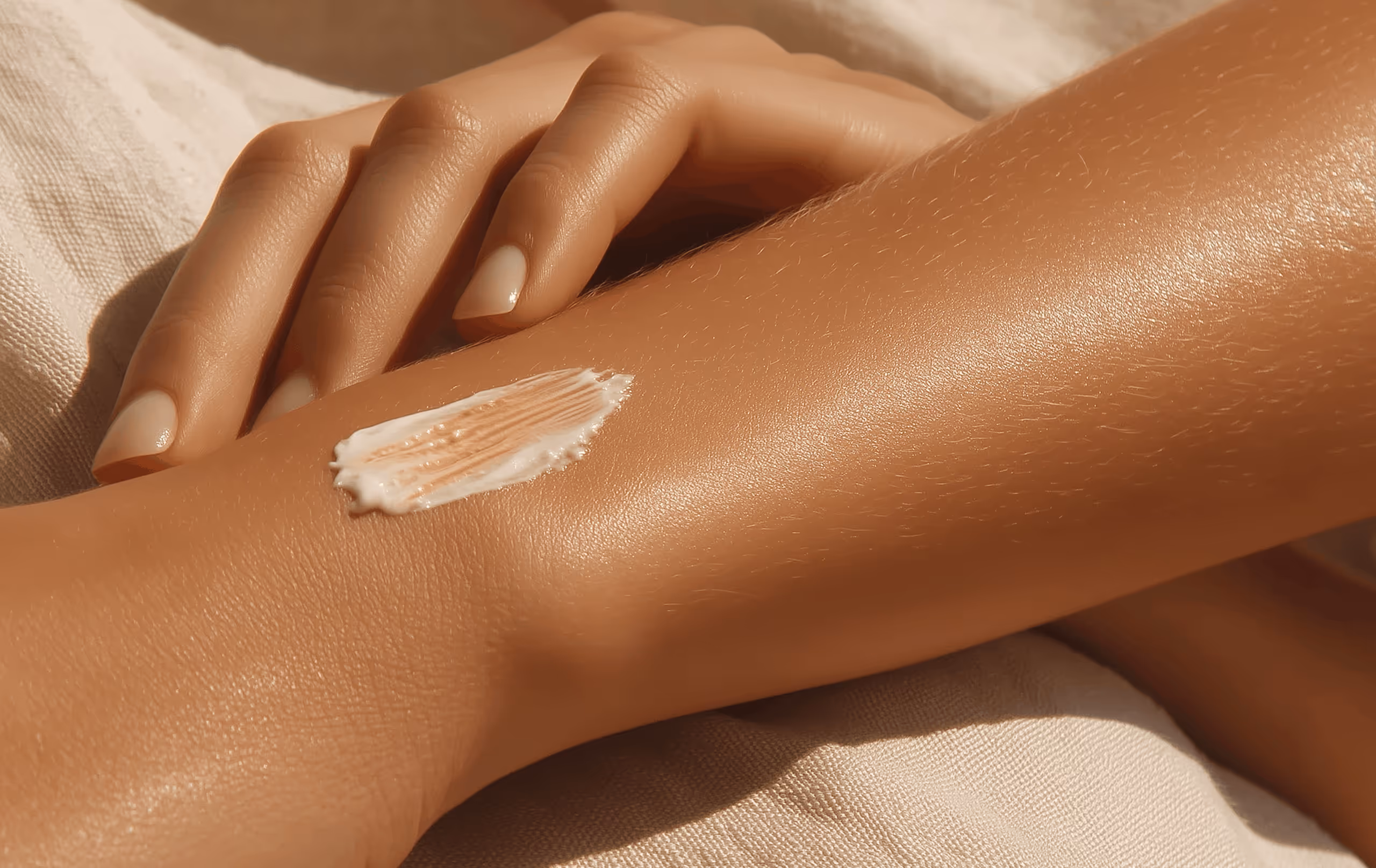 Hand gently resting on tanned leg with a smear of white cream on the skin.