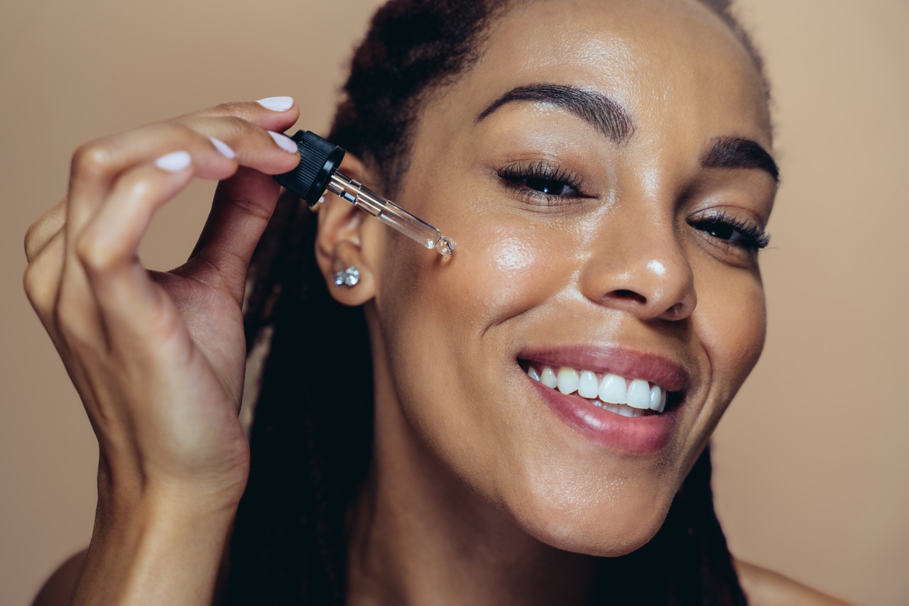 Woman applying serum with a dropper to glowing hydrated skin