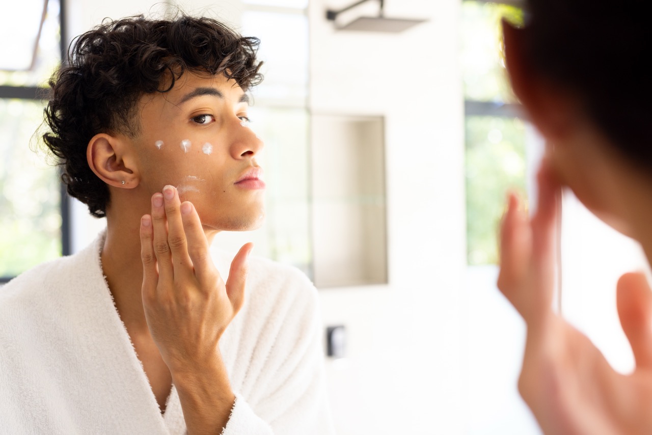 Man applying facial cream in the bathroom mirror as part of a skincare ritual