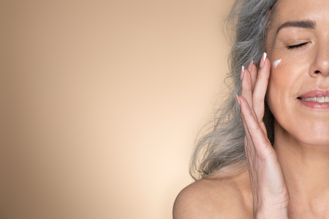 Woman with silver hair applying anti-aging cream to her cheek