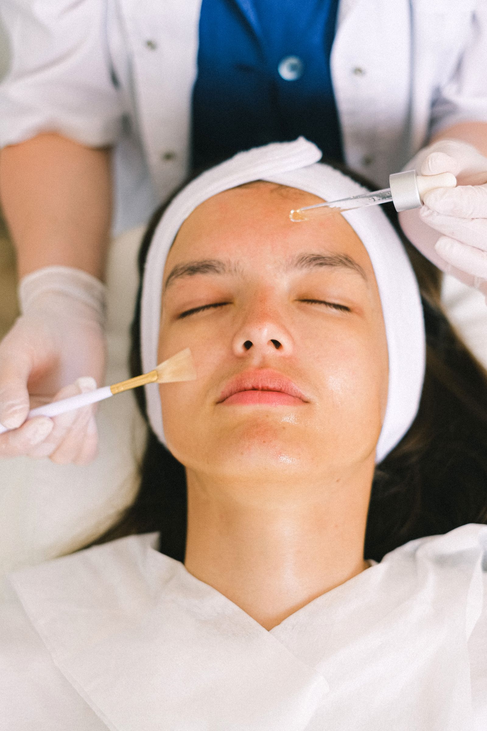 Aesthetician applying serum with a dropper and brush during a facial treatment