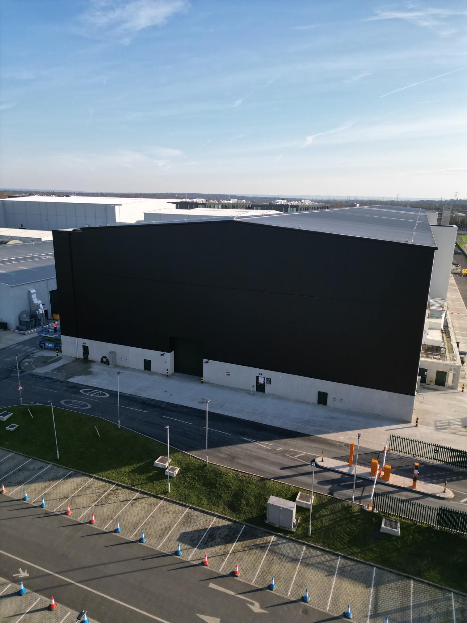 Large black and gray industrial warehouse building with adjacent parking and access road.