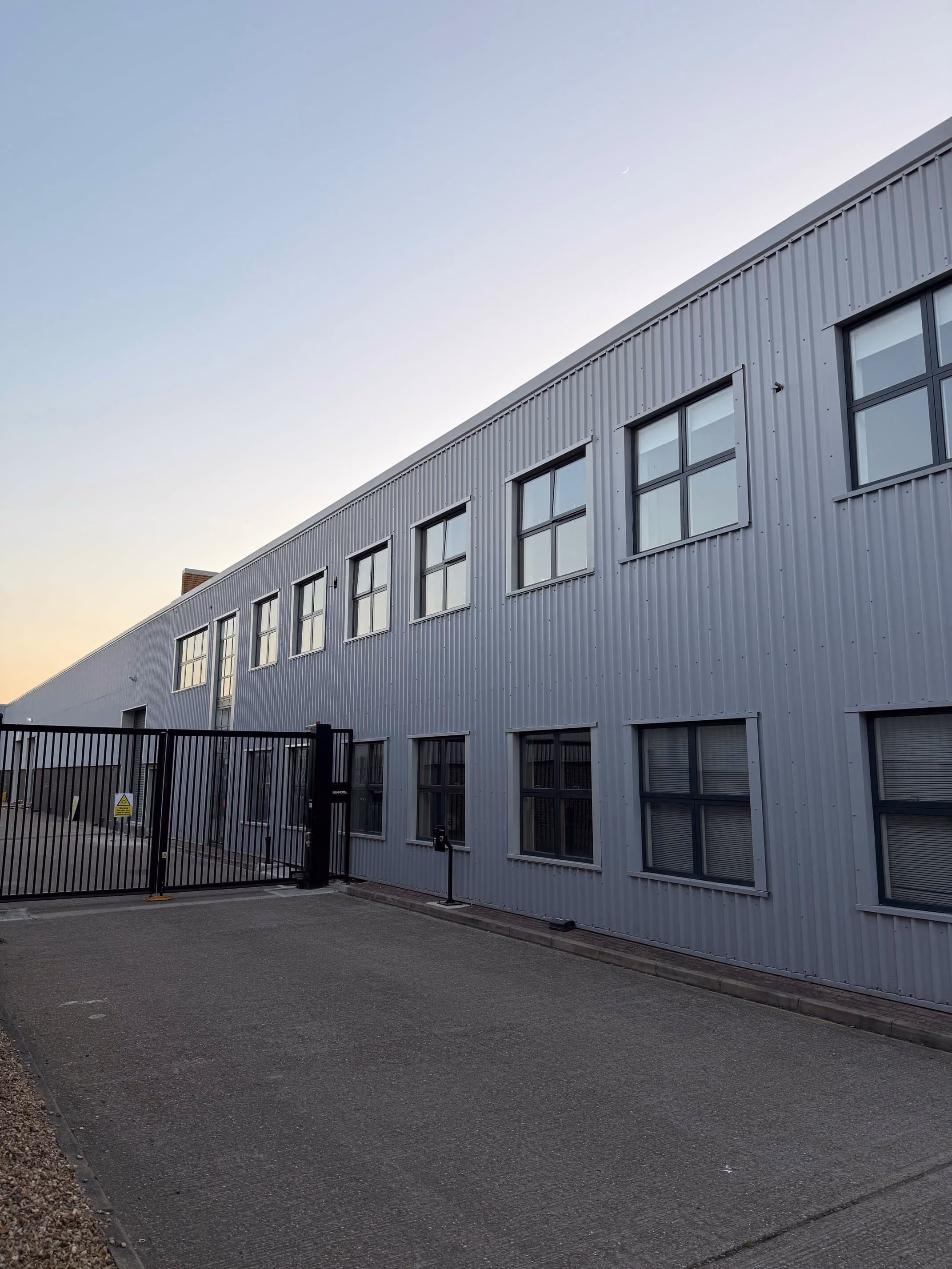 Gray industrial building with two rows of windows and a large black metal gate at the entrance.
