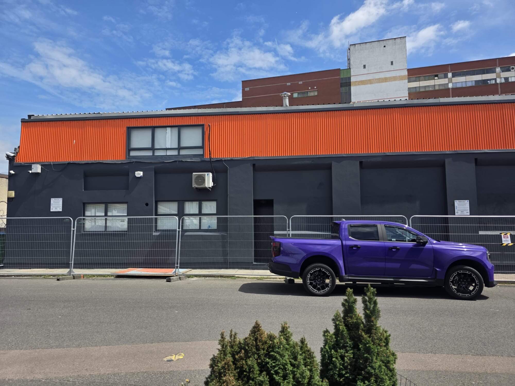 Purple pickup truck parked on street in front of a gray and orange building under a blue sky.