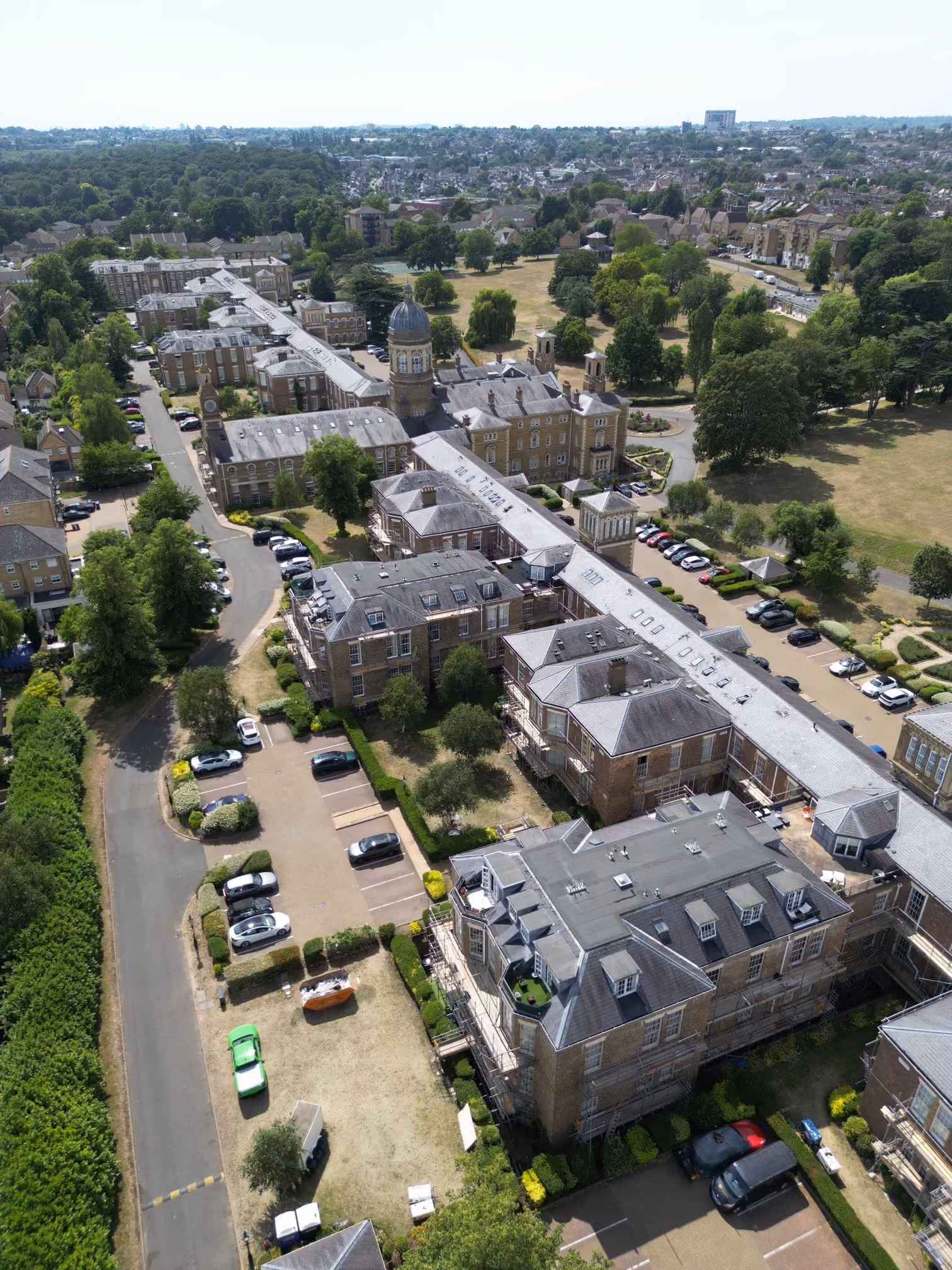 Aerial view of a historic brick building complex beside lawns and tree-lined roads.