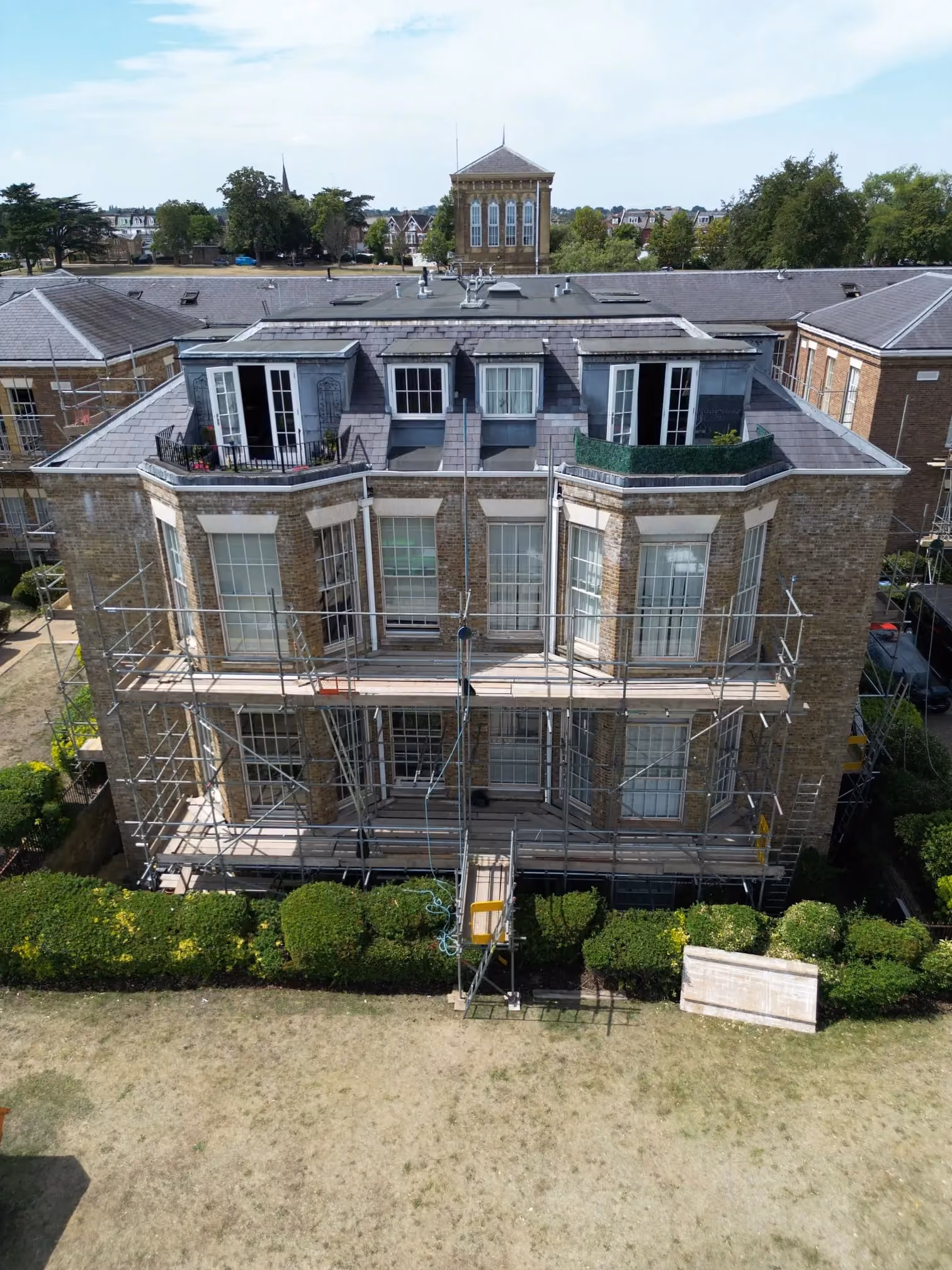 Scaffolding around a brick building with tall white sash windows and dormer windows.