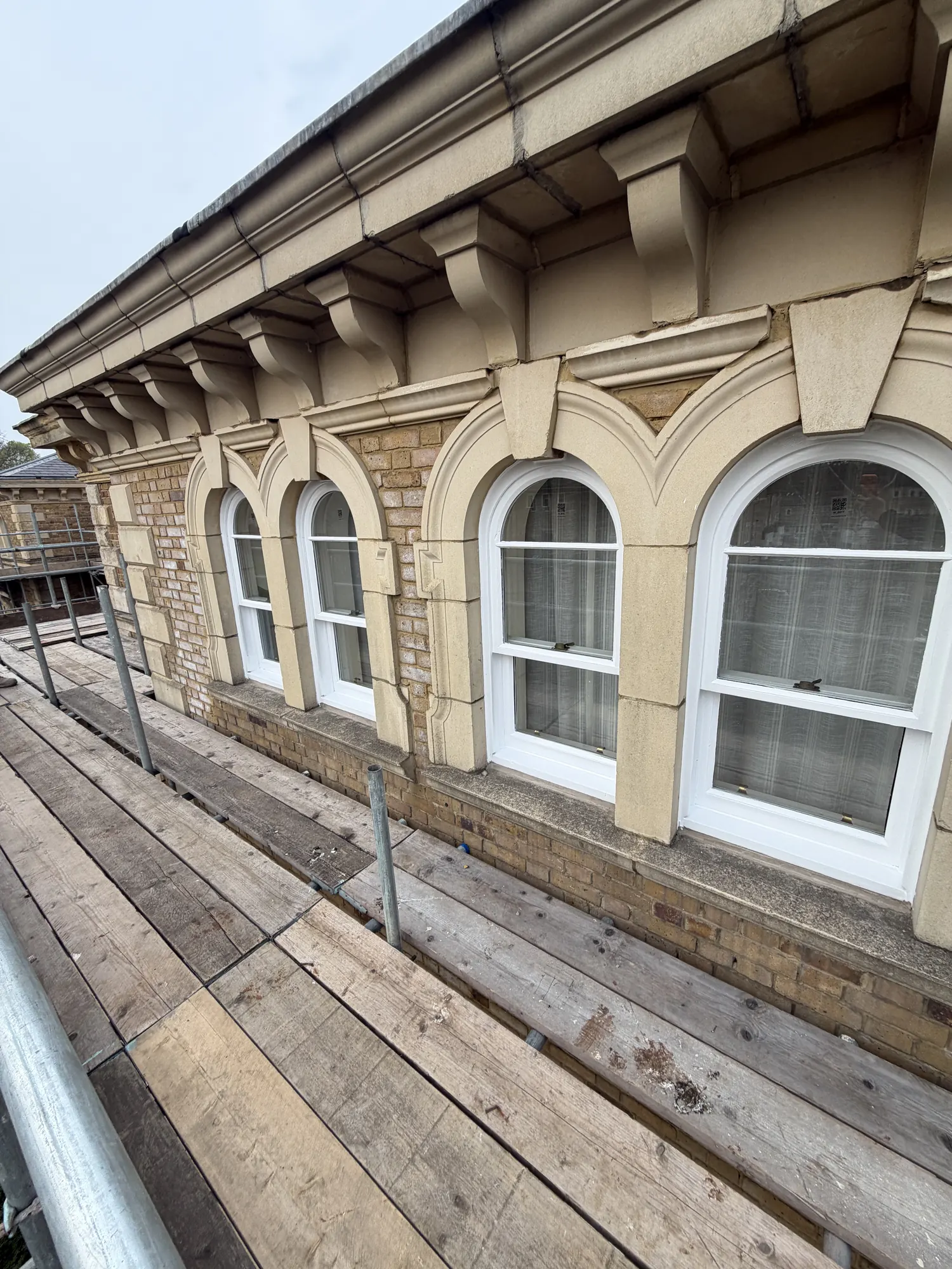 Row of white painted arched sash windows viewed from scaffold boards.
