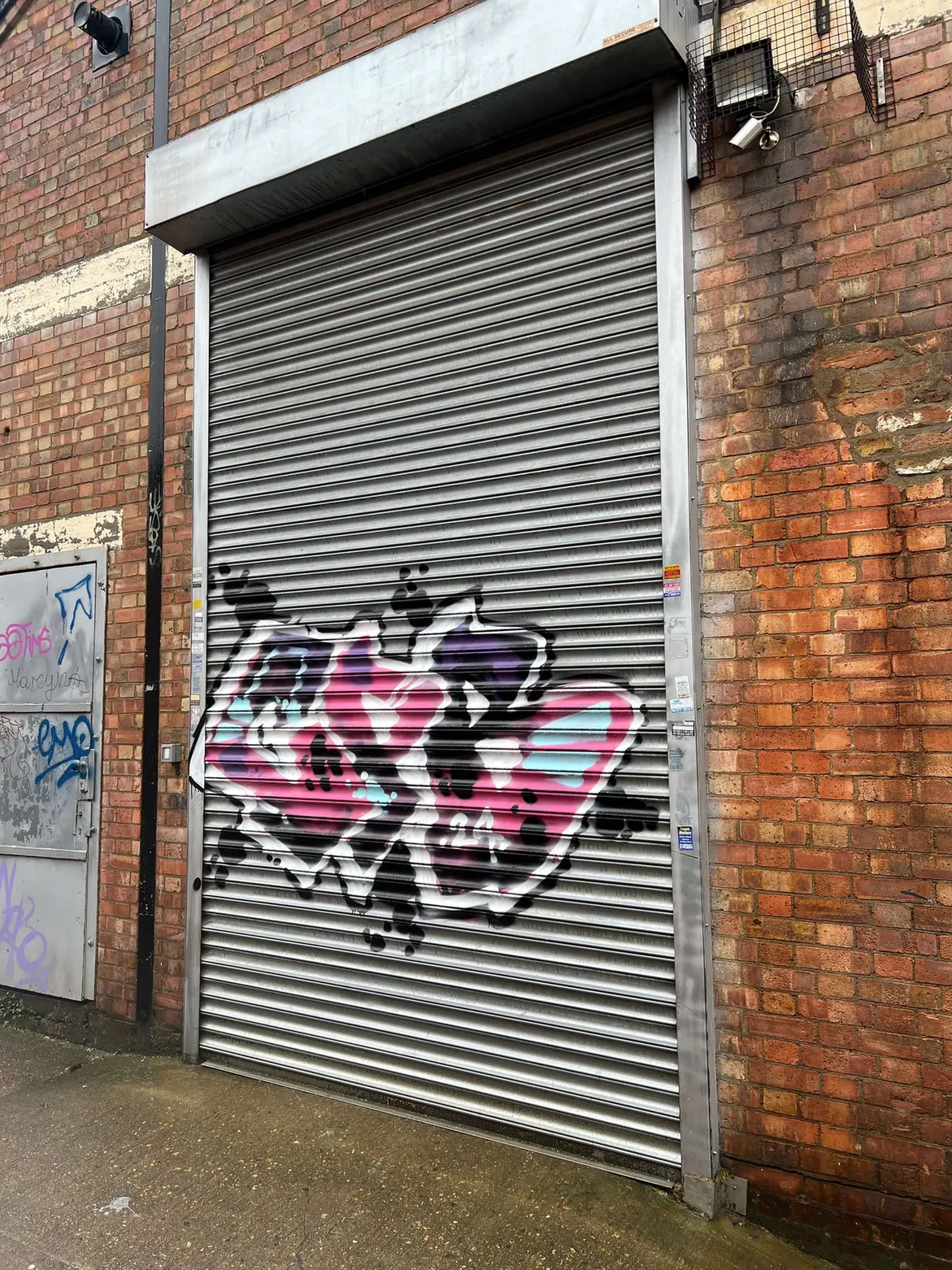 Graffiti on a metal roller shutter set into a brick wall.