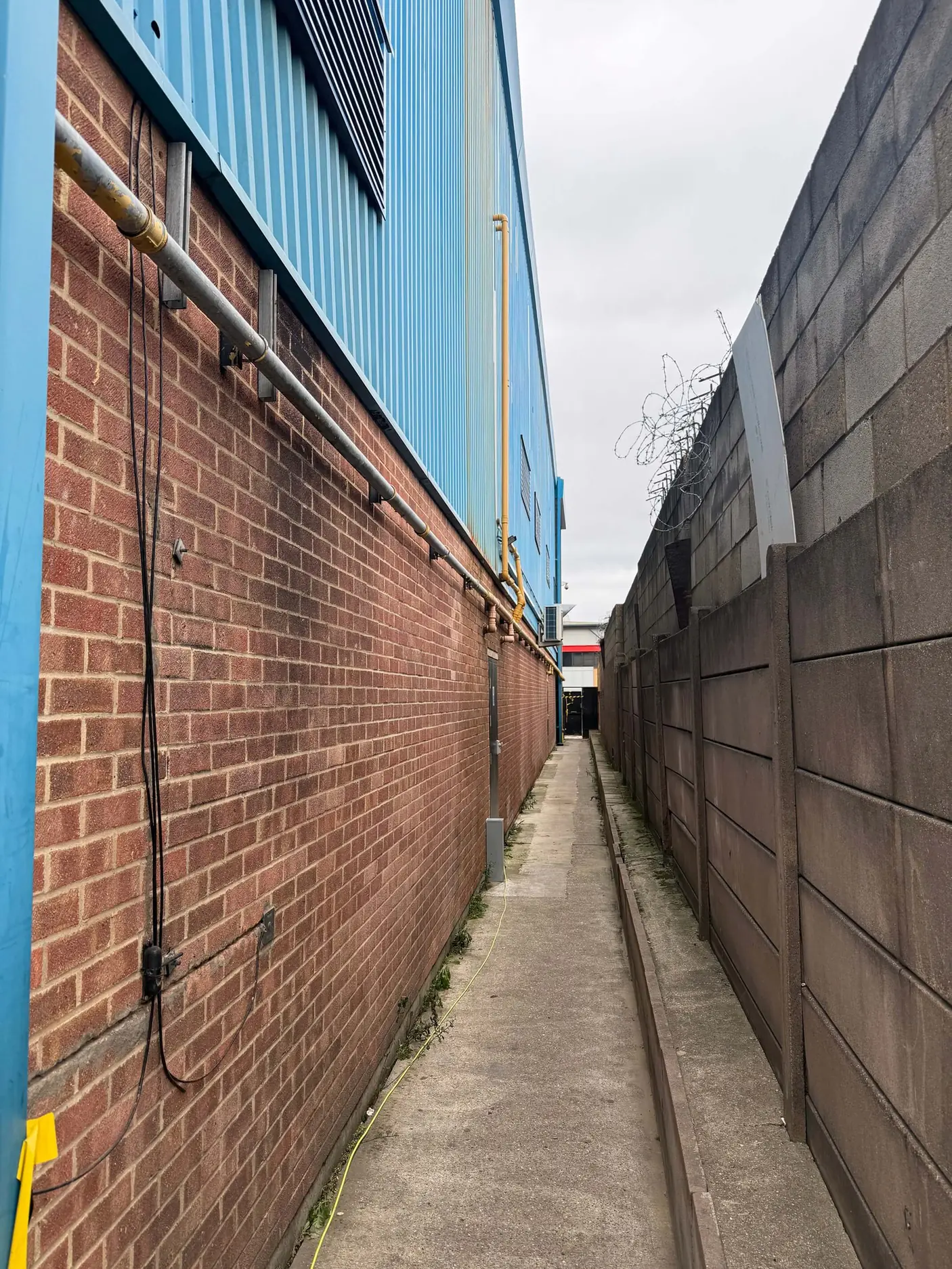 Blue metal cladding above brickwork and yellow pipework along a narrow access passage.