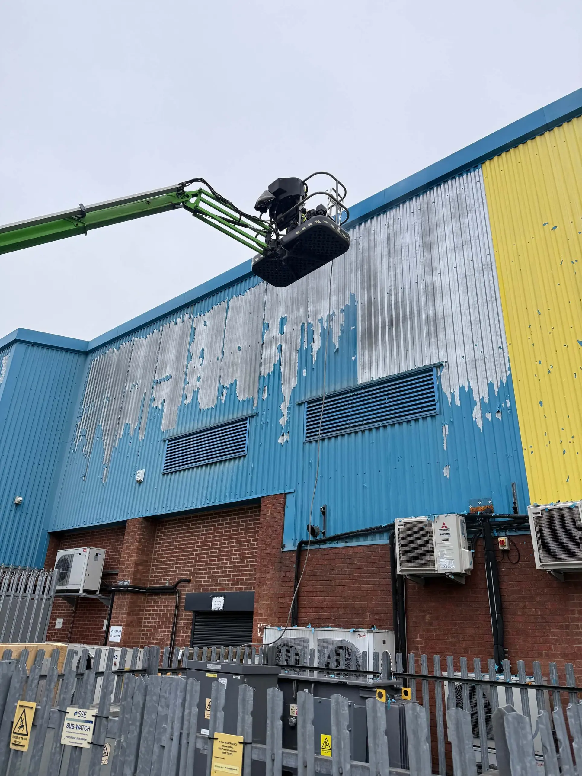 Worker on a boom lift preparing the upper section of blue industrial wall cladding.