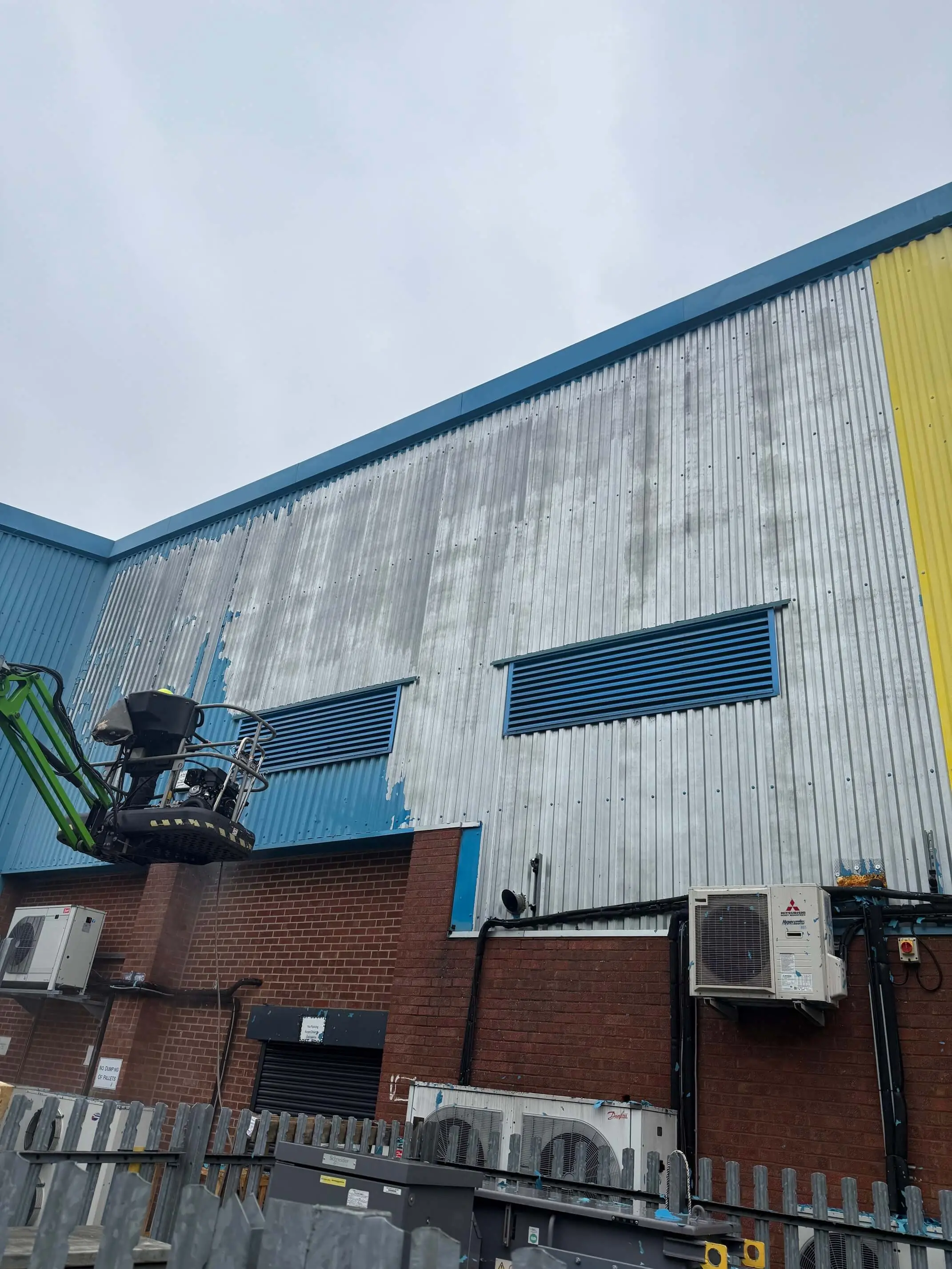 Partially stripped blue metal wall cladding above ventilation grilles and air-conditioning units.