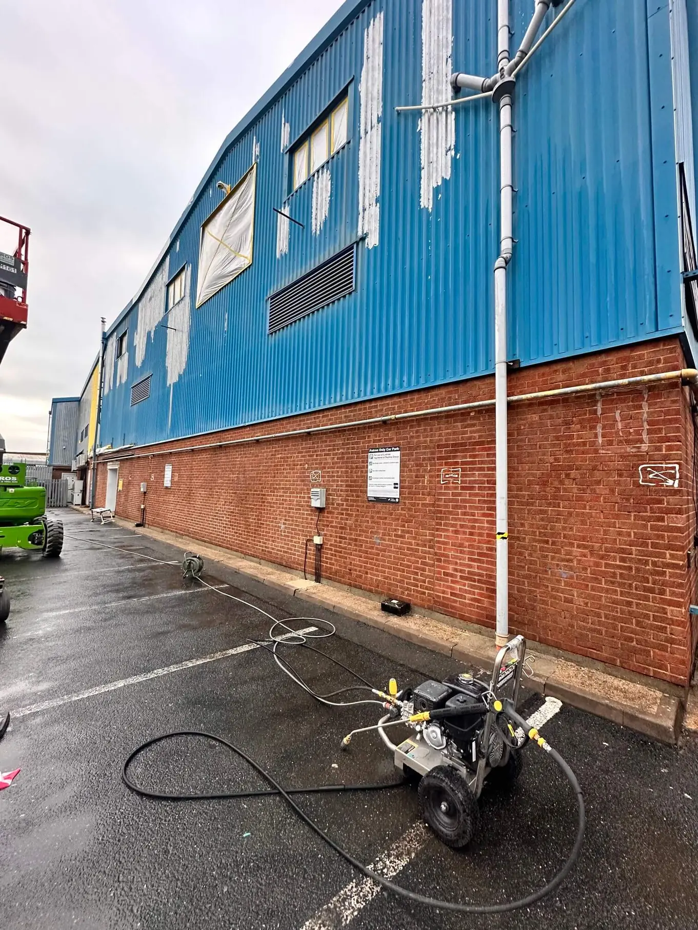 Outdoor industrial area with blue and brick building and a pressure washer on wet asphalt.