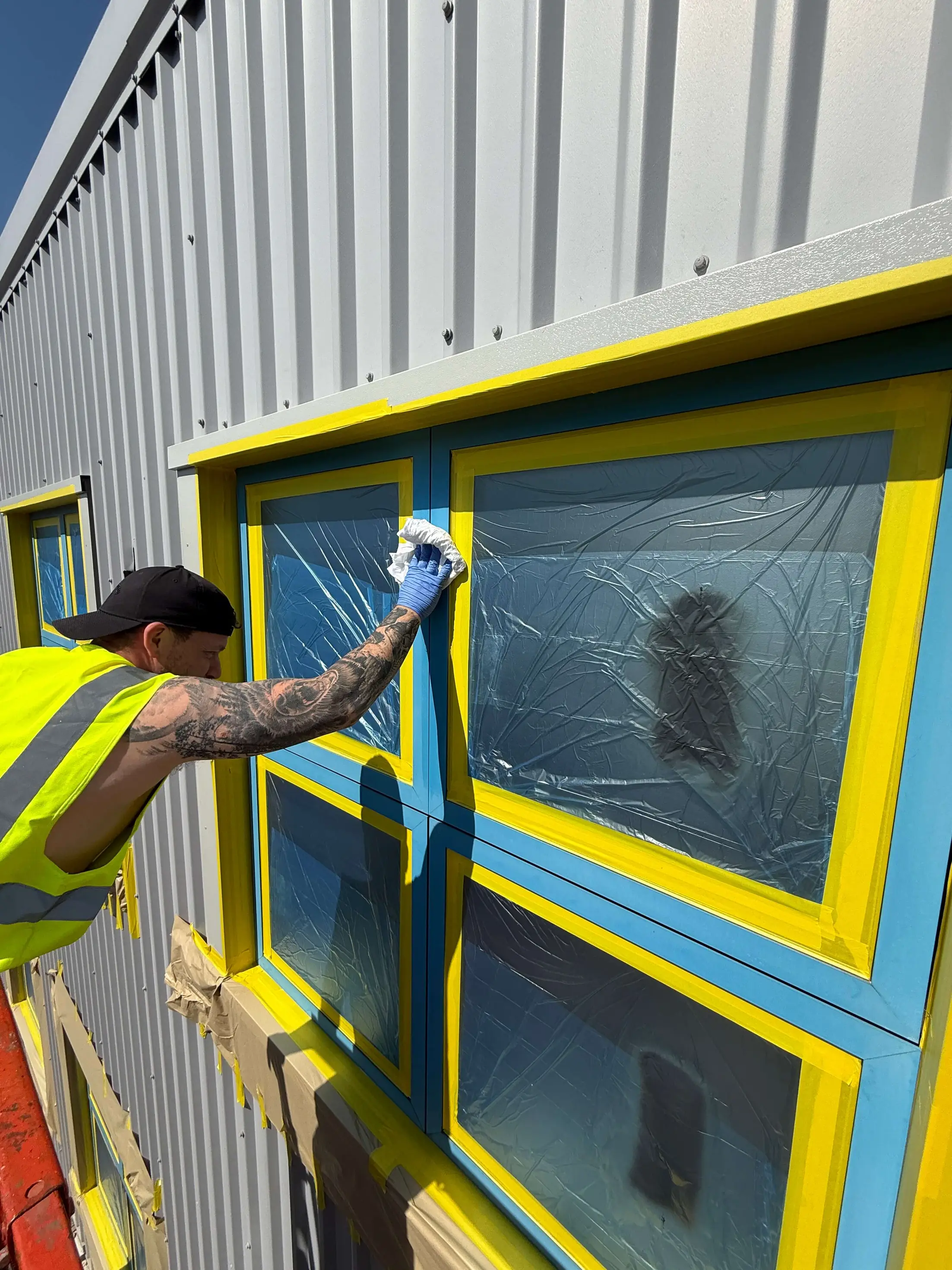Worker wiping a blue aluminium window frame with the glazing masked