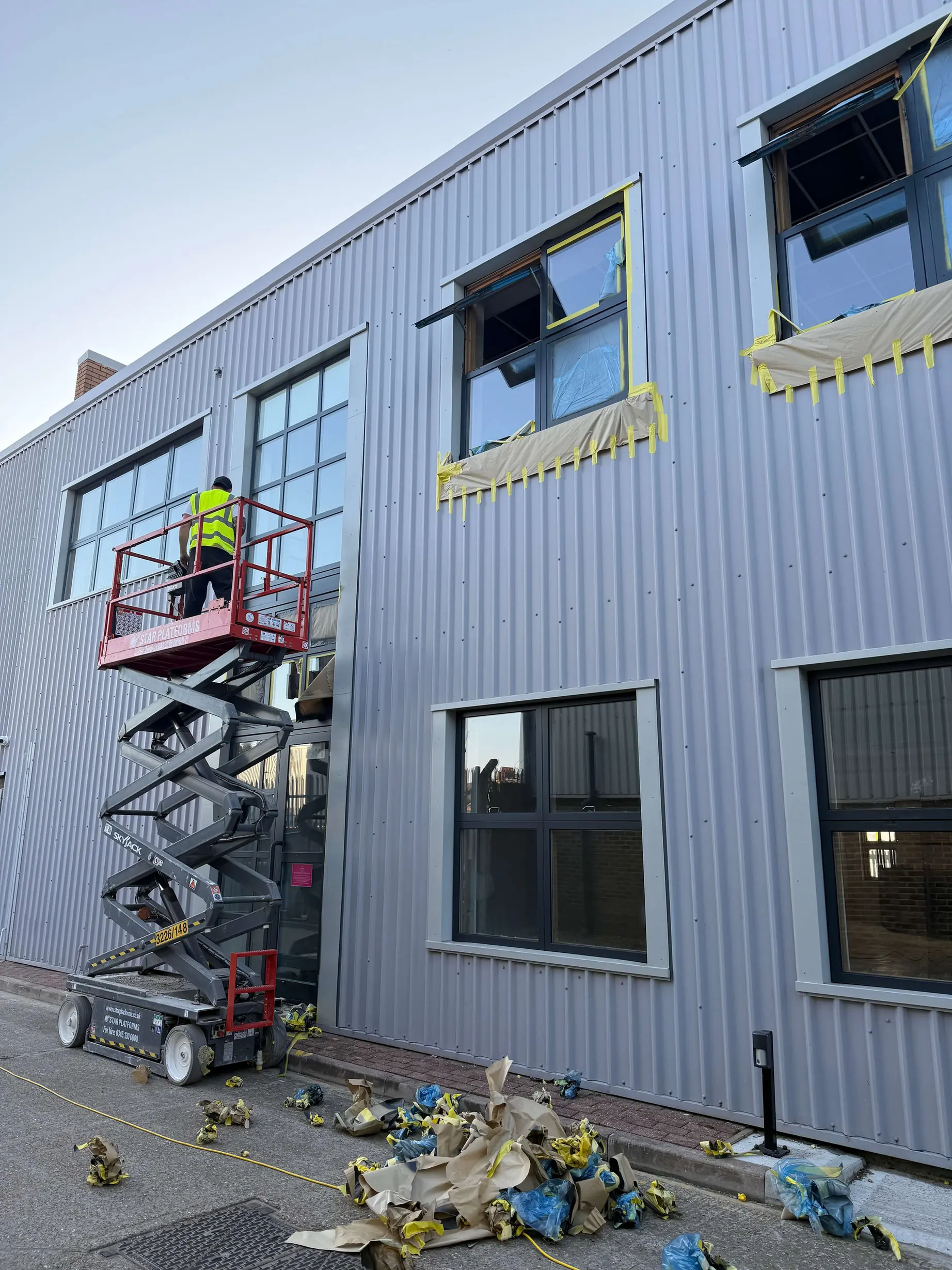Worker on a scissor lift beside masked upper-floor windows