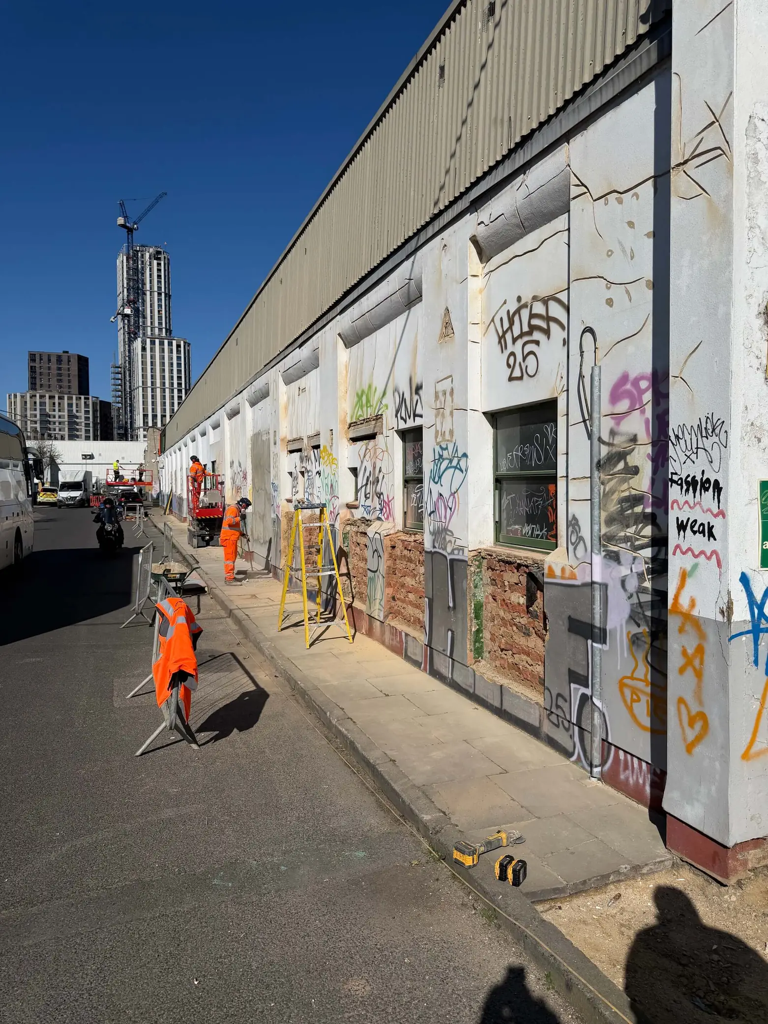 Graffiti-covered industrial frontage with workers and access equipment on the pavement.