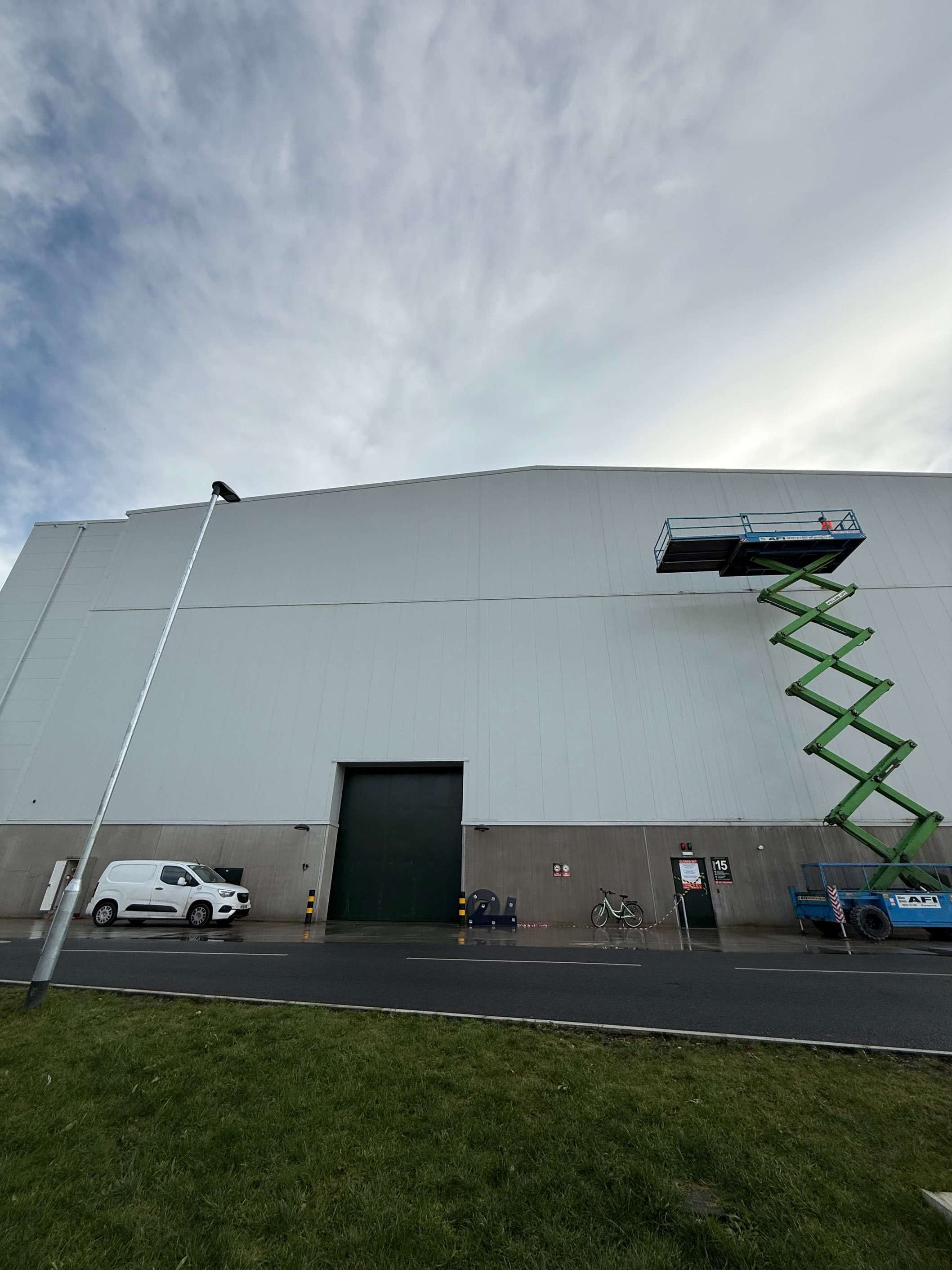Raised scissor lift beside the light-coloured cladding of a large industrial building.