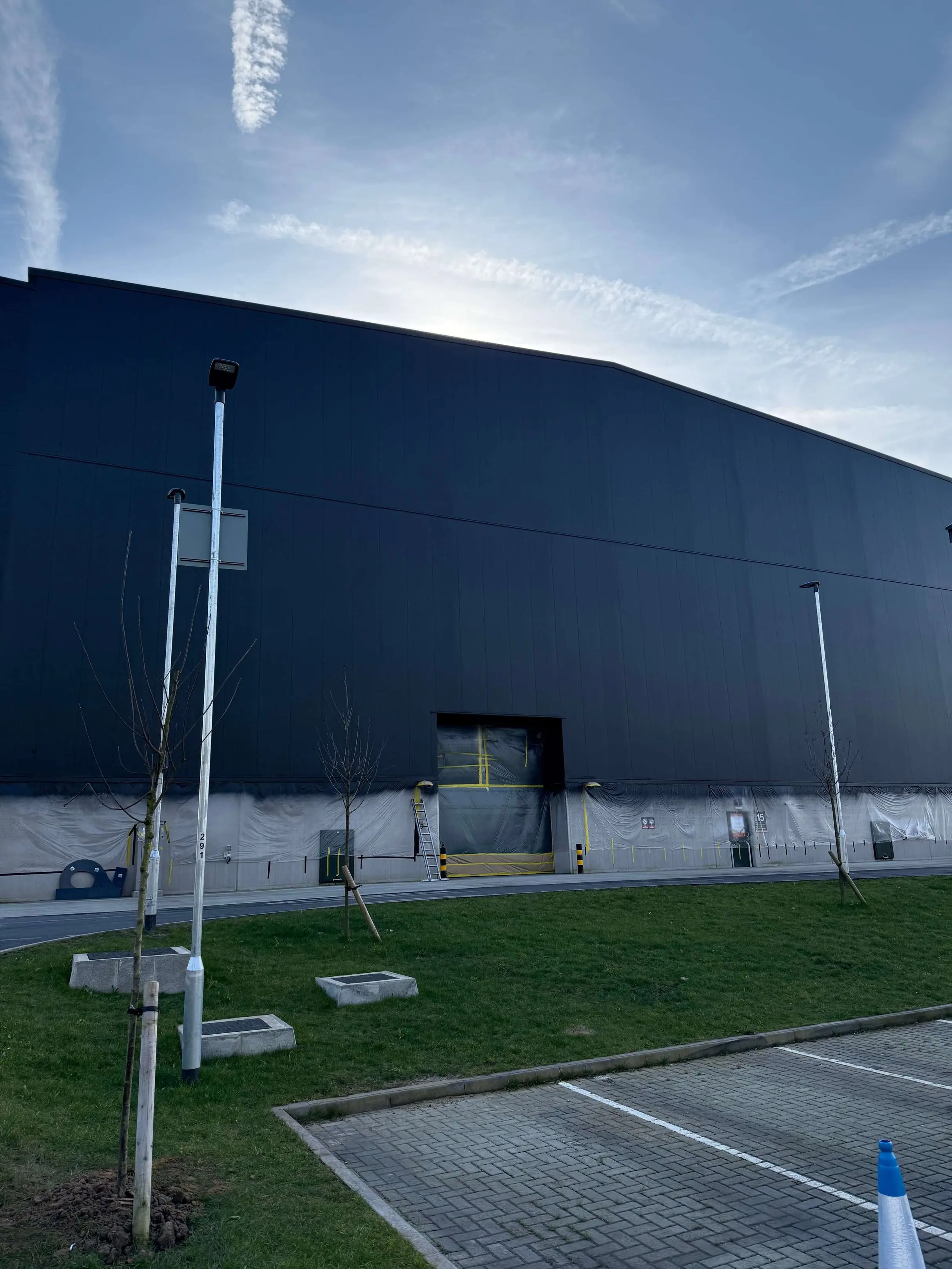 Dark-coated industrial wall cladding above a protected work area and grass verge.