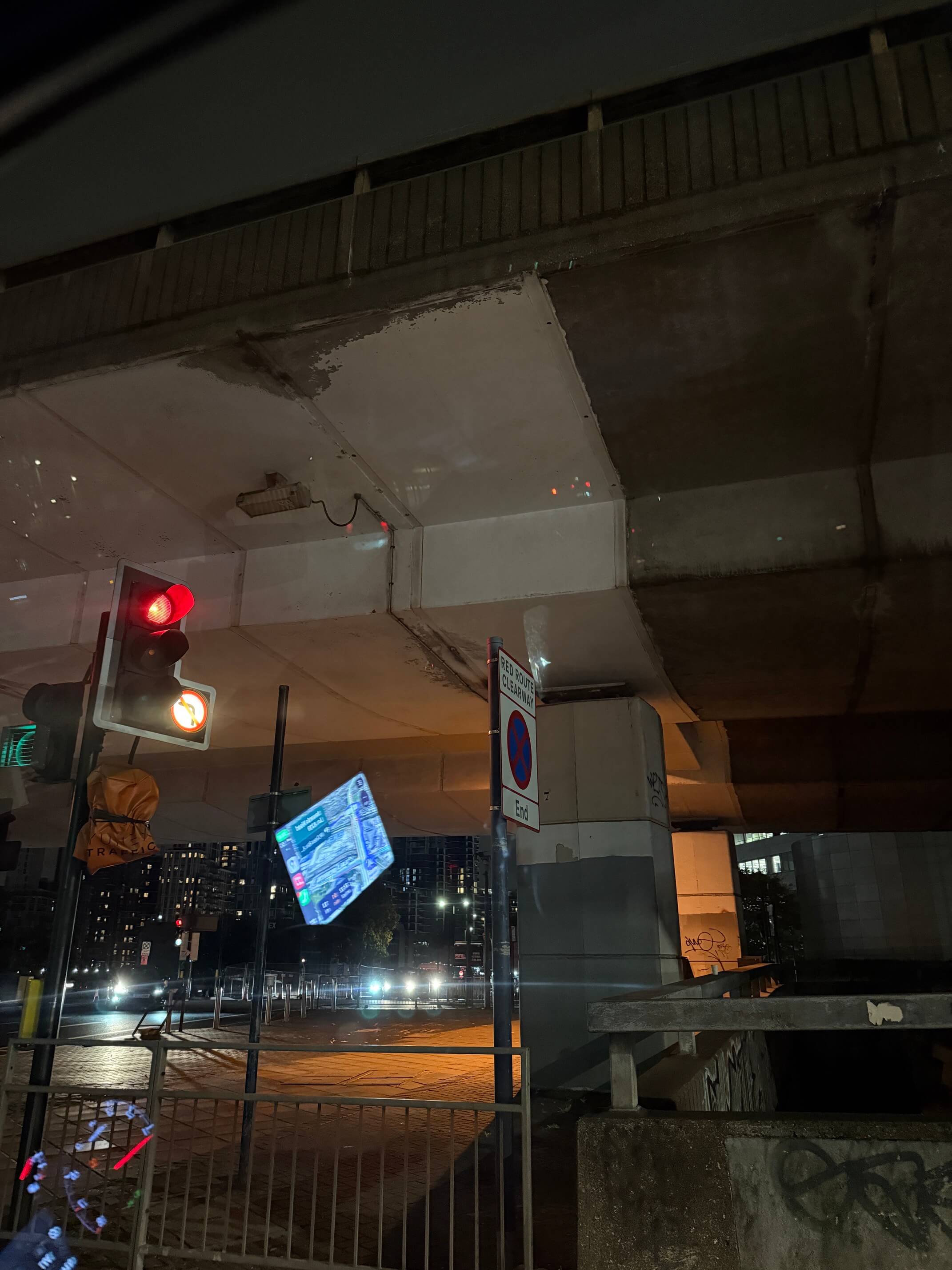 Night scene under a concrete overpass with a red traffic light and a no parking sign.