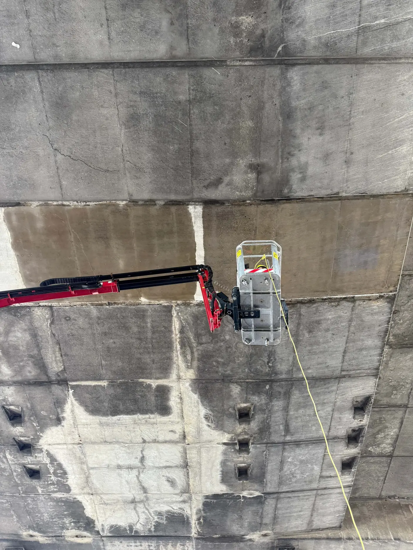 Worker pressure-washing the underside of a concrete bridge from a raised access platform.