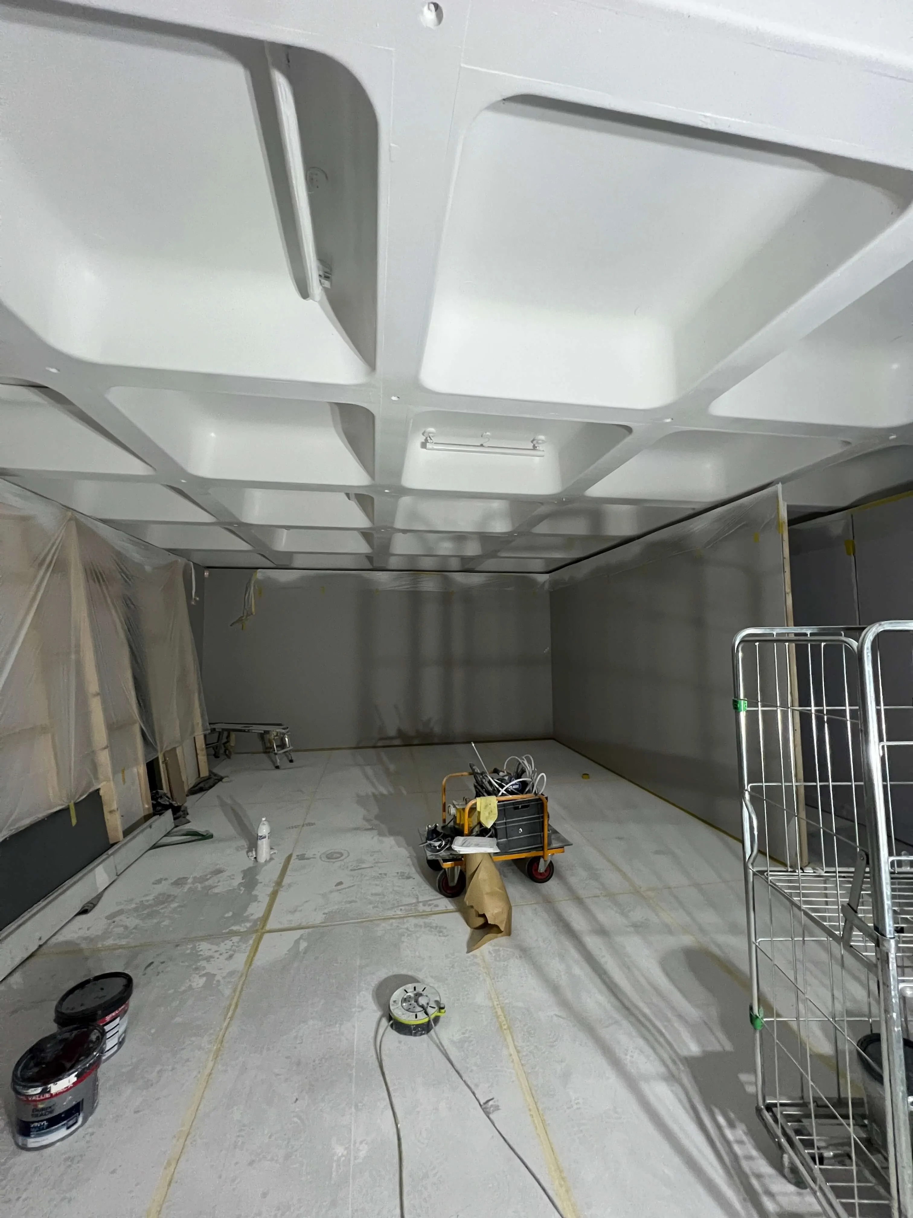 White coffered ceiling above a masked room with floor protection and coating equipment.